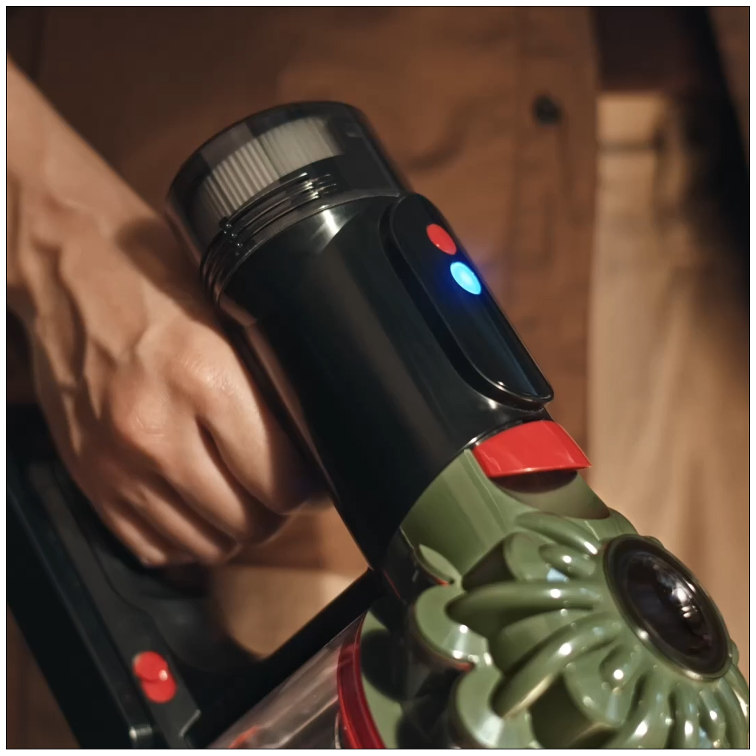 Une main saisit un aspirateur noir et vert avec des voyants bleu et rouge.