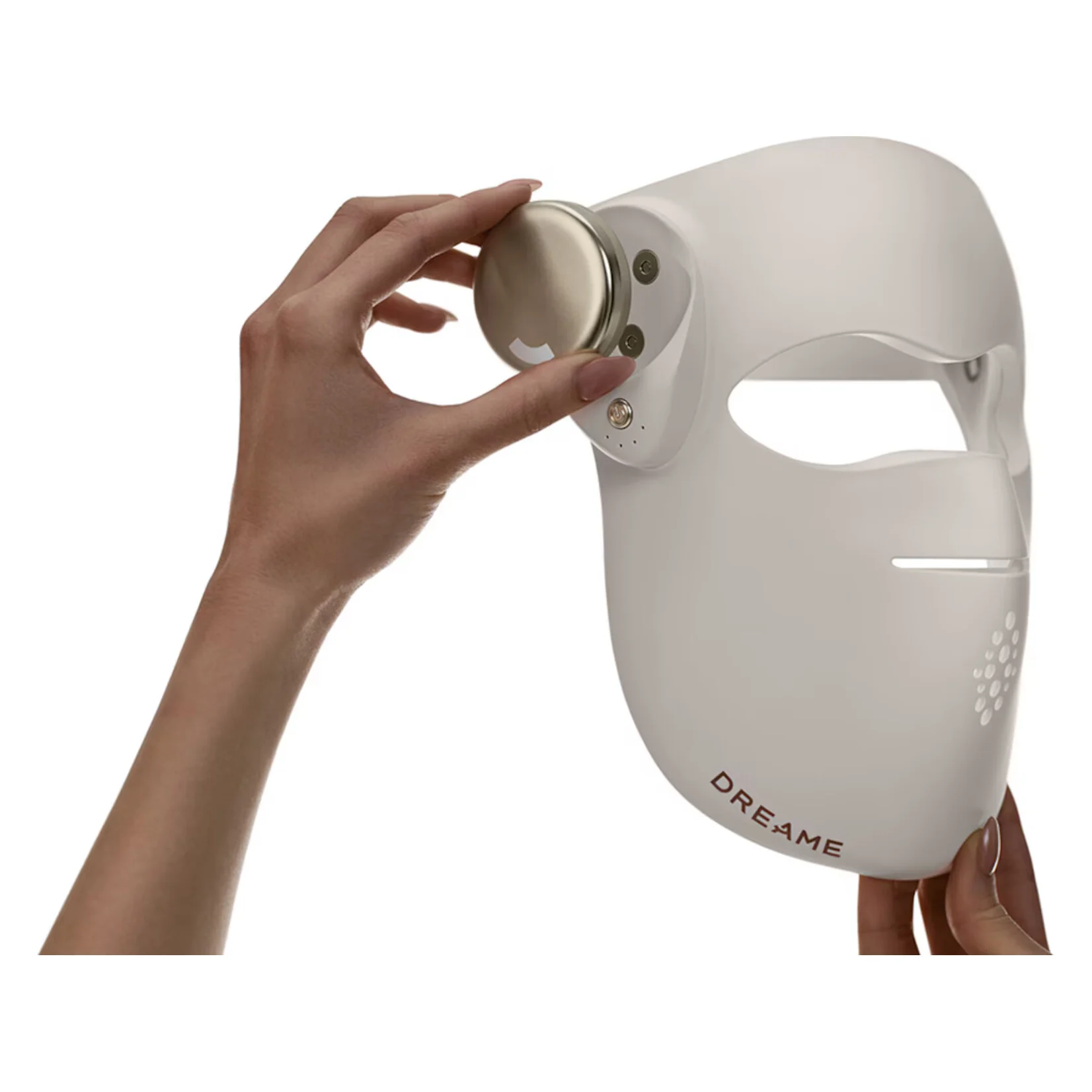 Una mano sostiene una mascarilla facial blanca con un dial dorado.