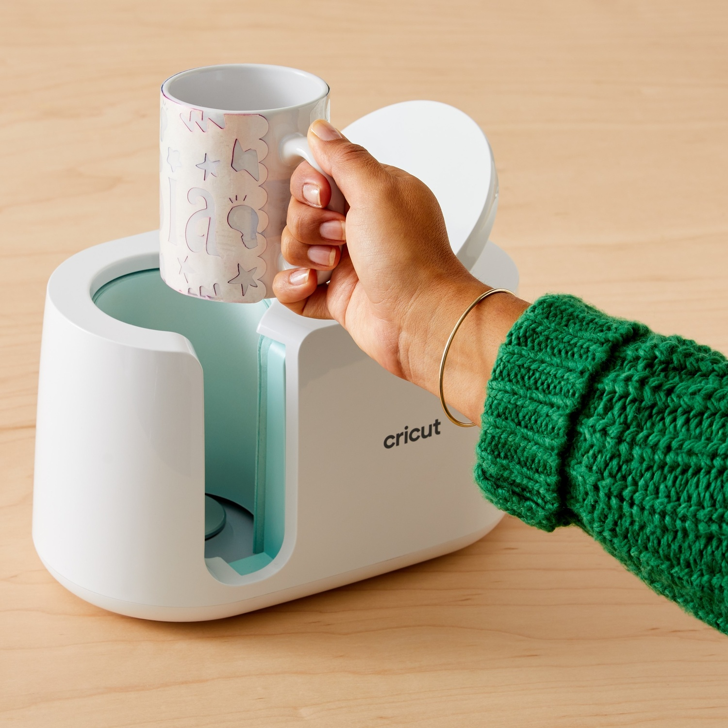 Una mano posiziona una tazza a motivi in una macchina Cricut bianca.
