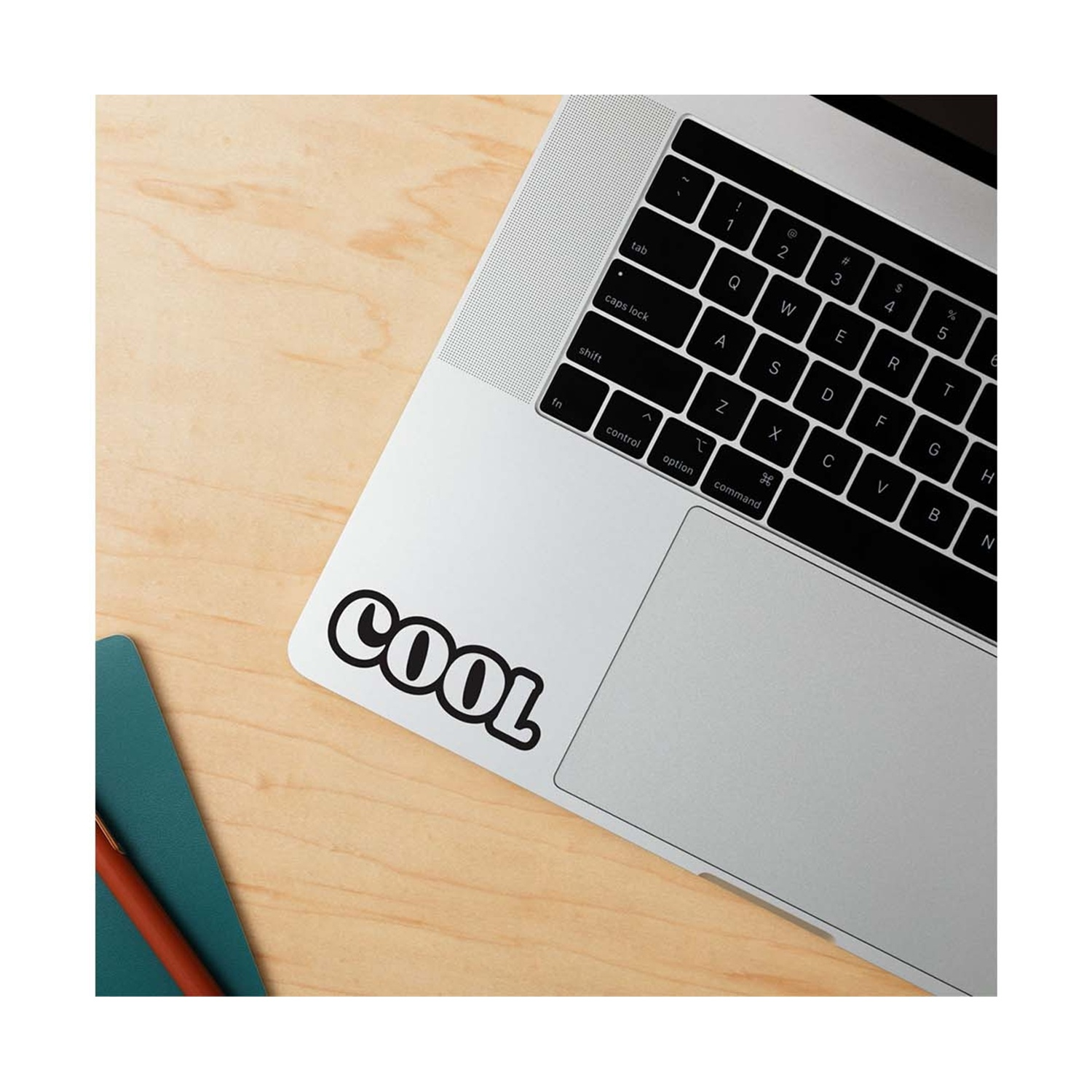 Un laptop con un adesivo "COOL", accanto a un quaderno verde e una penna.