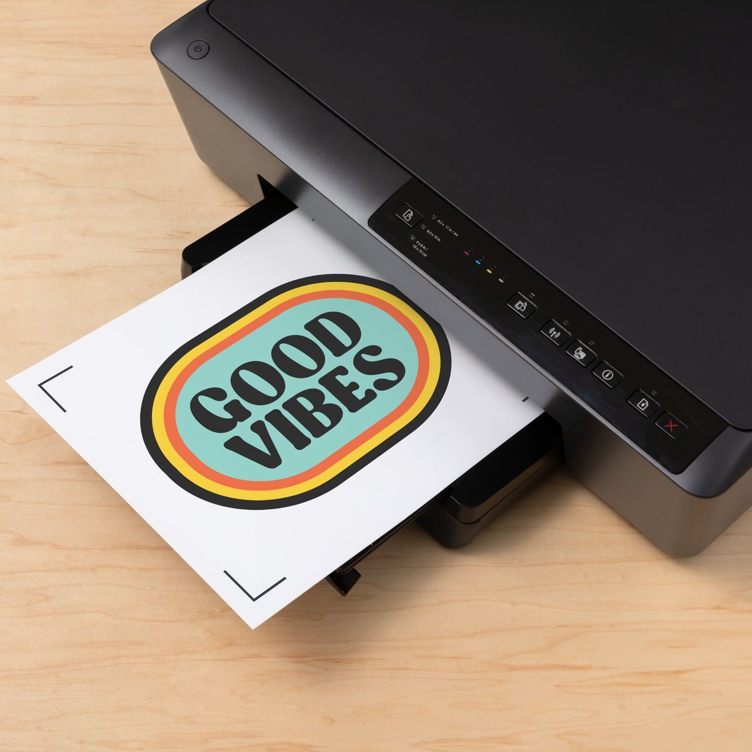 Una stampante nera stampa un foglio con "GOOD VIBES" in un design ovale colorato.