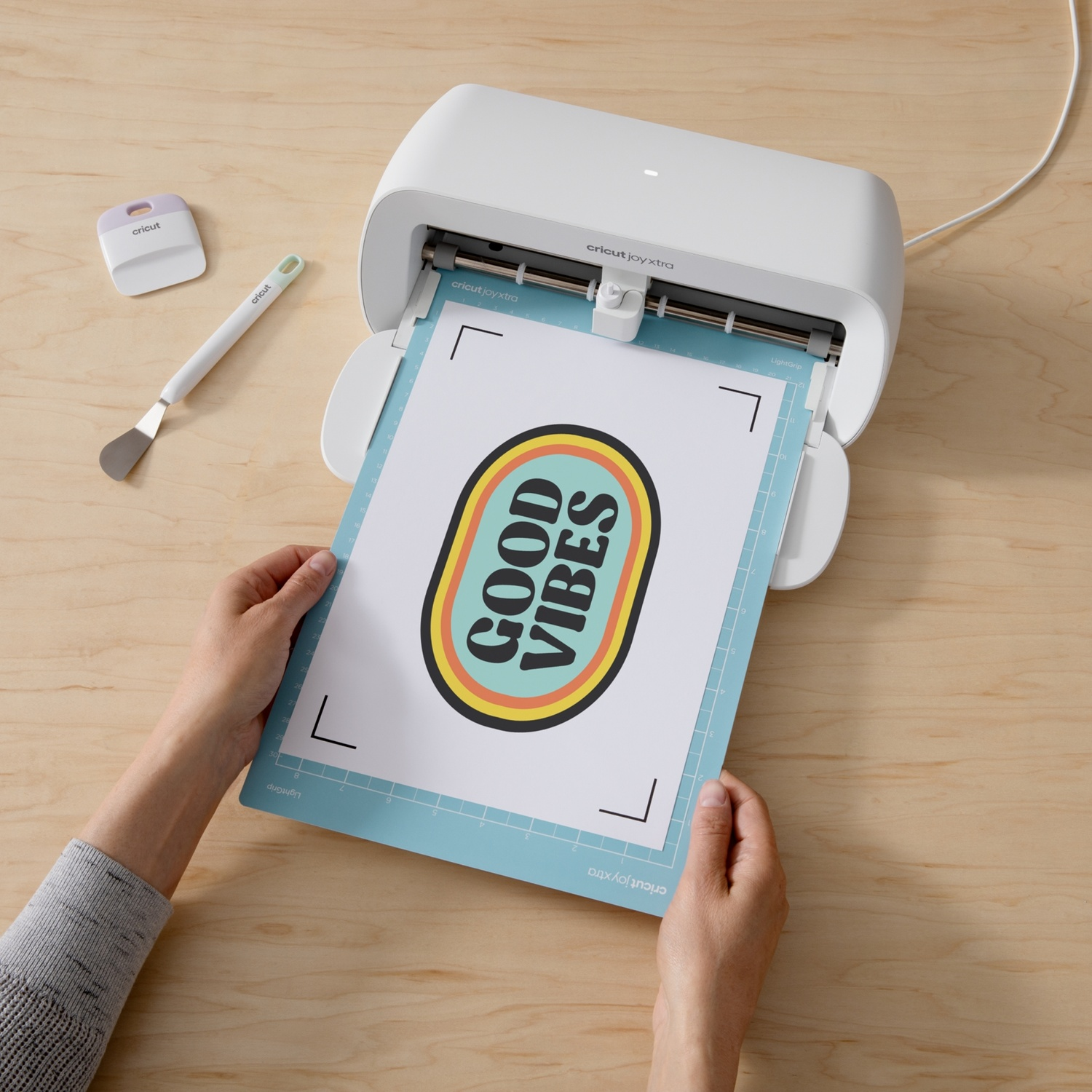 Le mani posizionano un adesivo "GOOD VIBES" in una macchina da taglio Cricut Joy Xtra.