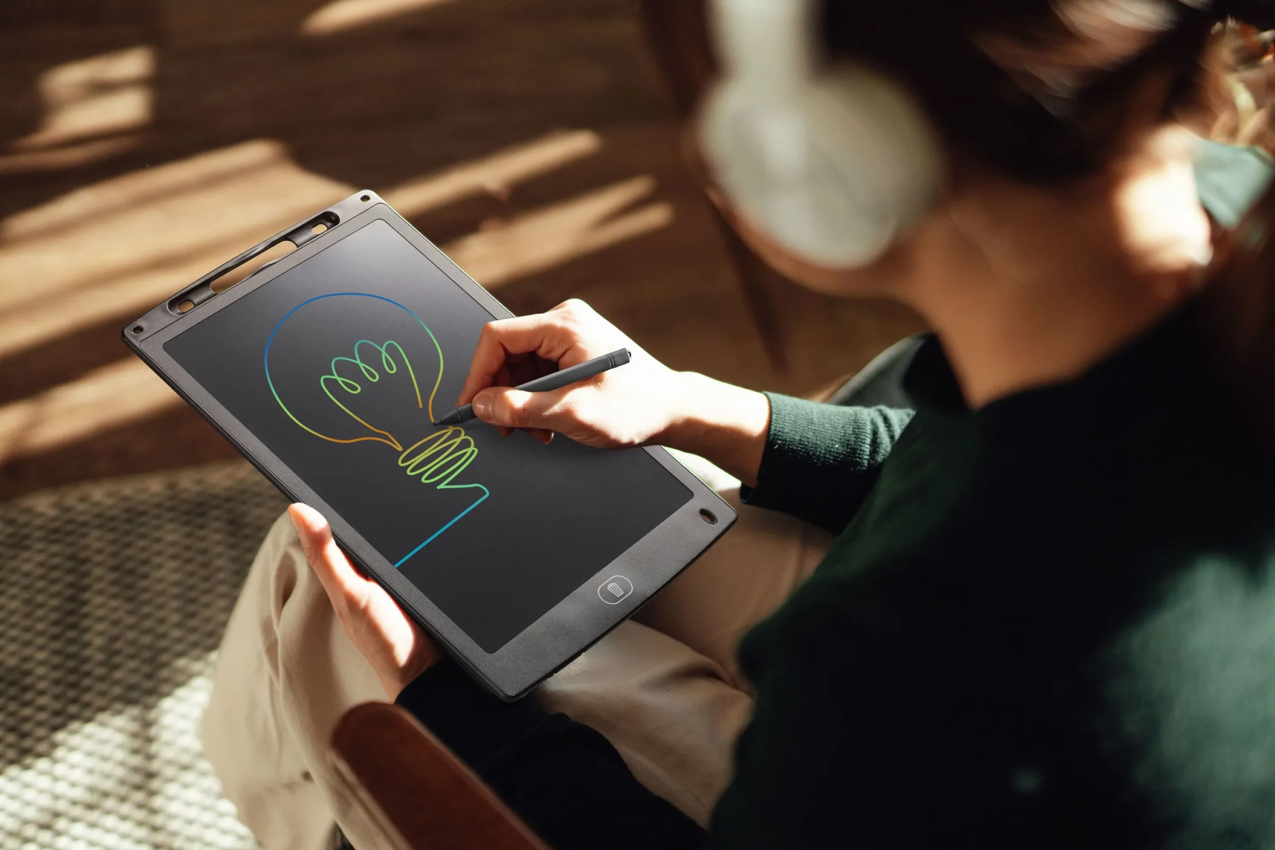 Eine Person mit Kopfhörern zeichnet eine Glühbirne auf einem digitalen Tablet.