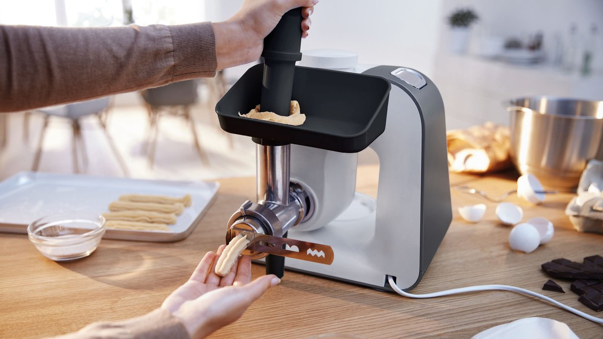 Ręka używa robota kuchennego do wyciskania ciasta przez ukształtowaną dyszę.