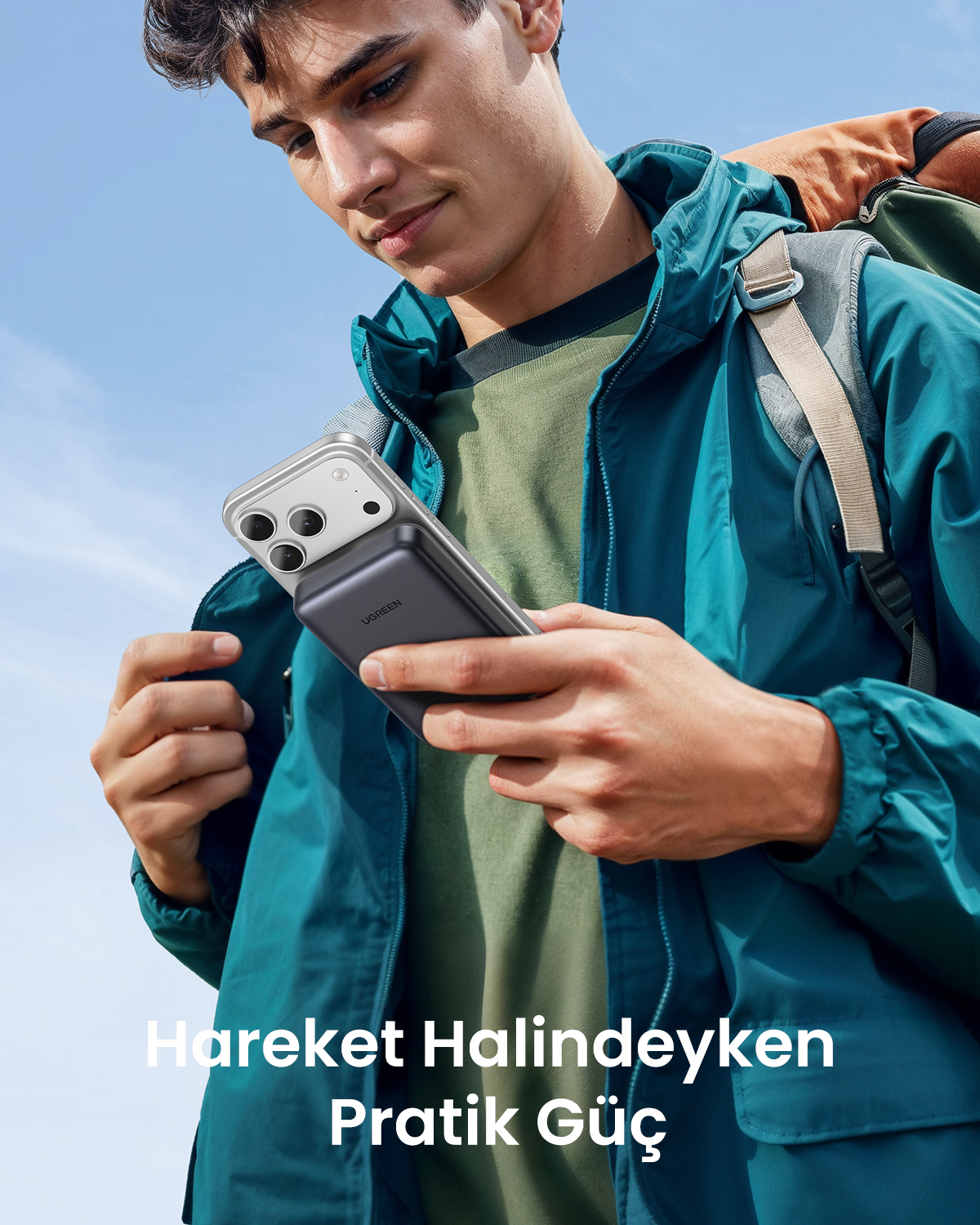 Erkek telefonunu powerbank ile tutuyor. Arkada mavi gökyüzü.