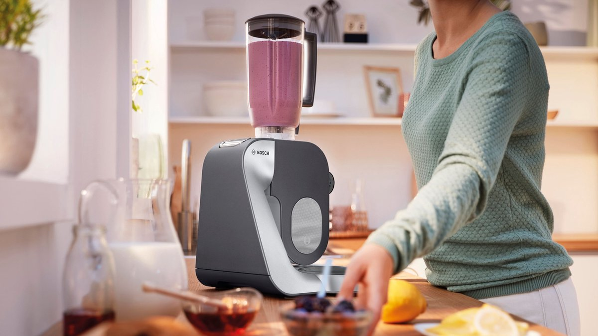Kobieta w zielonym swetrze używa blendera Bosch z różowym smoothie.