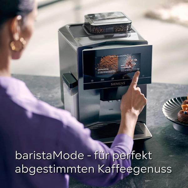 Eine Frau bedient eine Kaffeemaschine mit Touchscreen. Kaffeebohnen sind sichtbar.