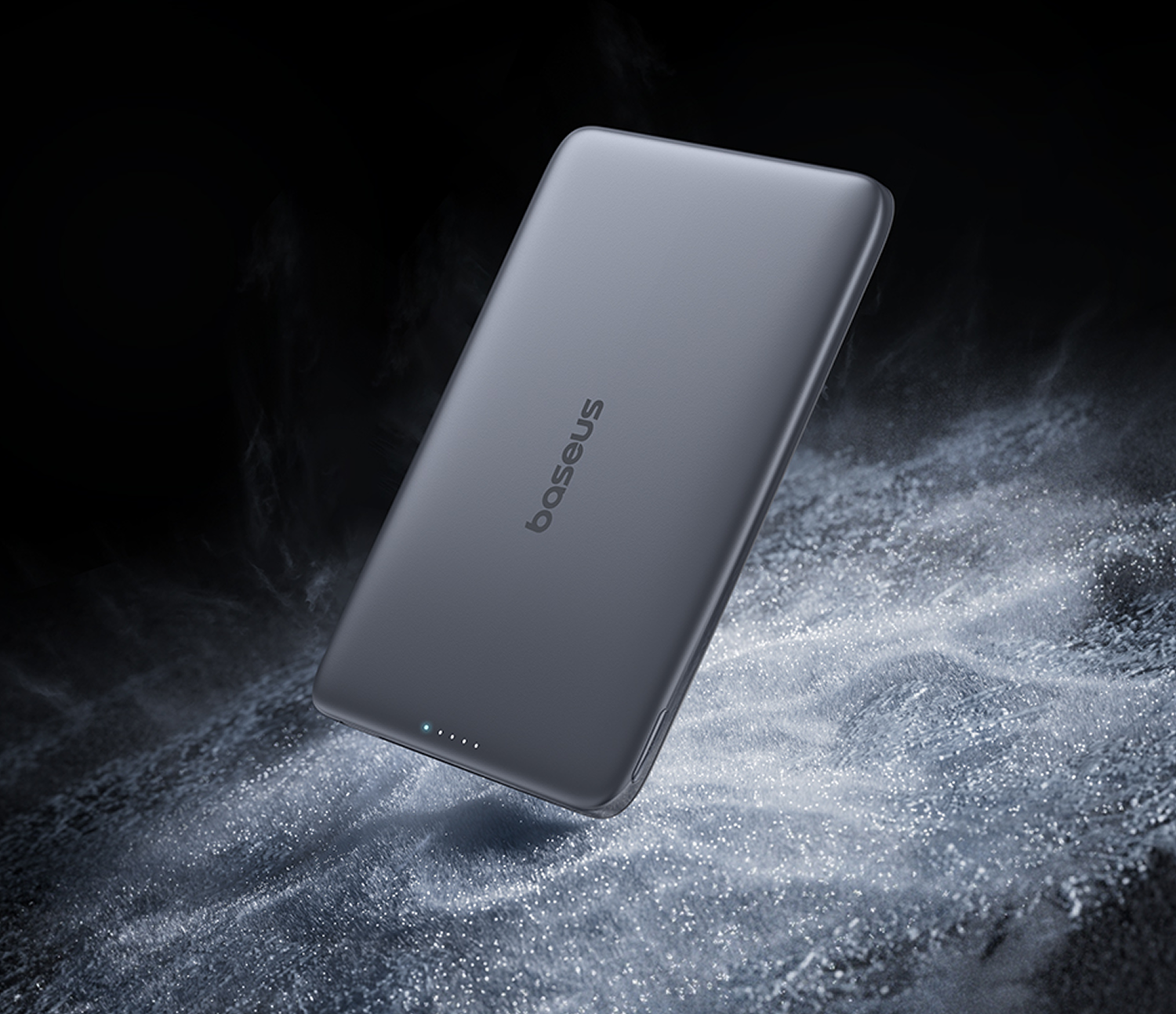 Una batería externa Baseus gris oscuro descansa sobre una superficie texturizada oscura con polvo blanco.
