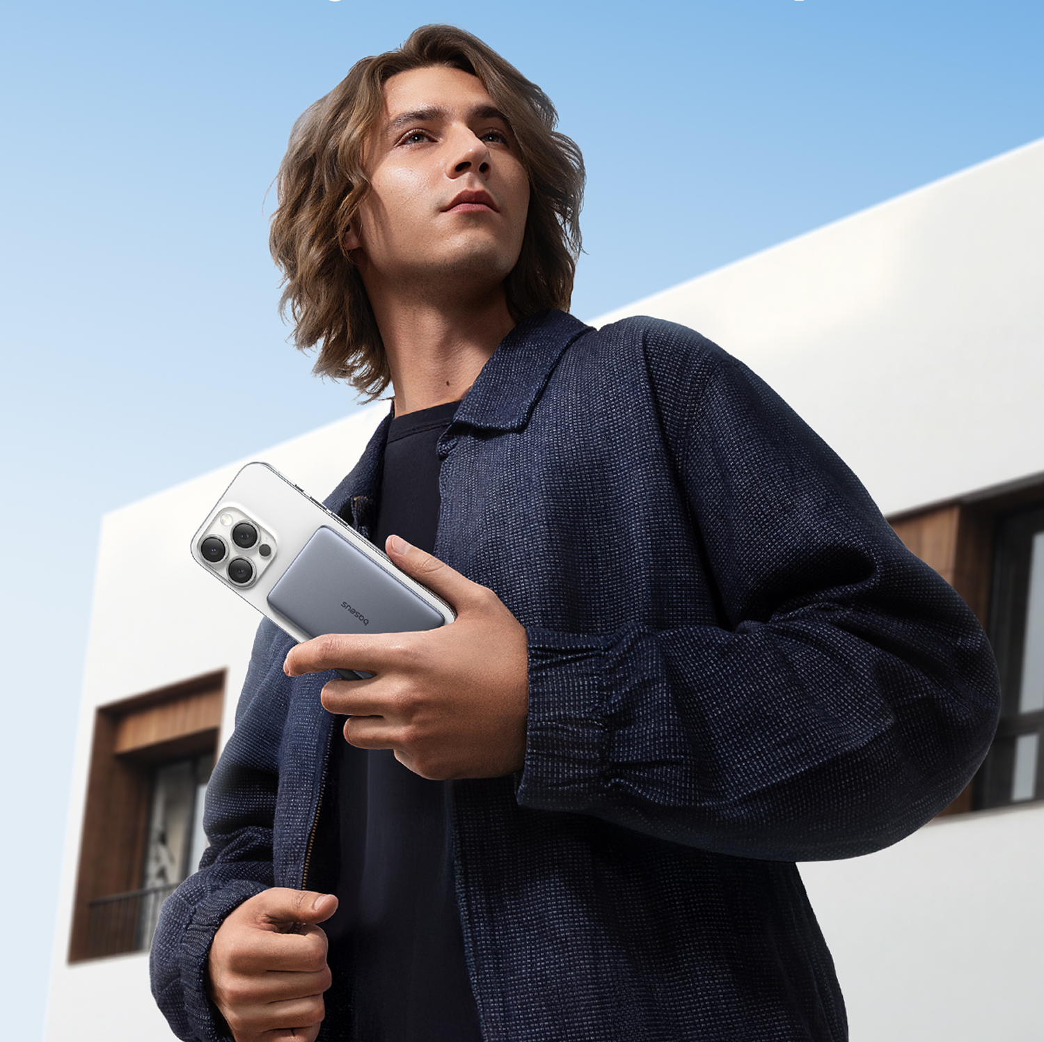 Hombre de pelo largo sostiene un smartphone frente a un edificio moderno.