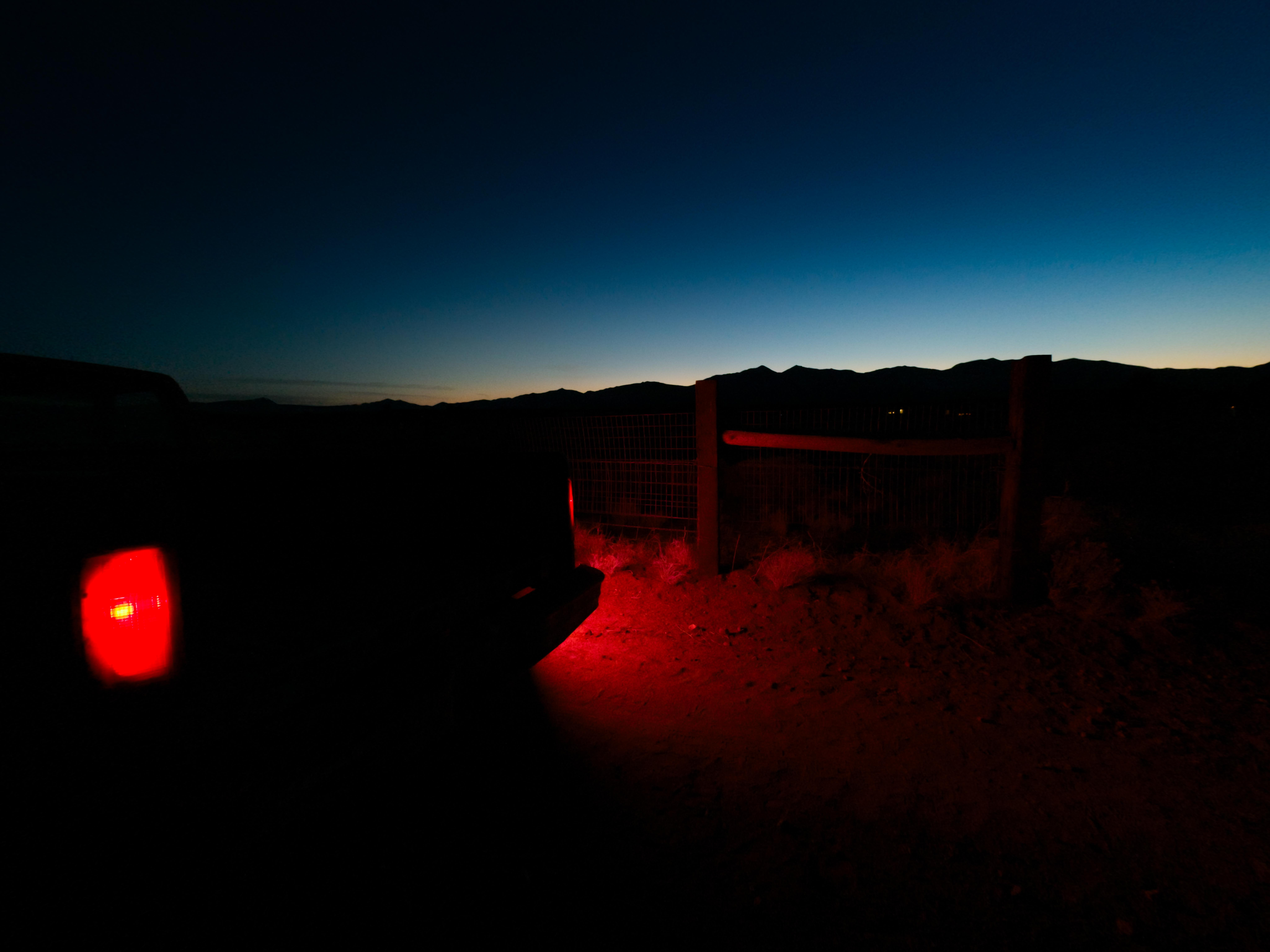 Rotes Rücklicht beleuchtet den Boden bei Dämmerung neben einem Zaun.
