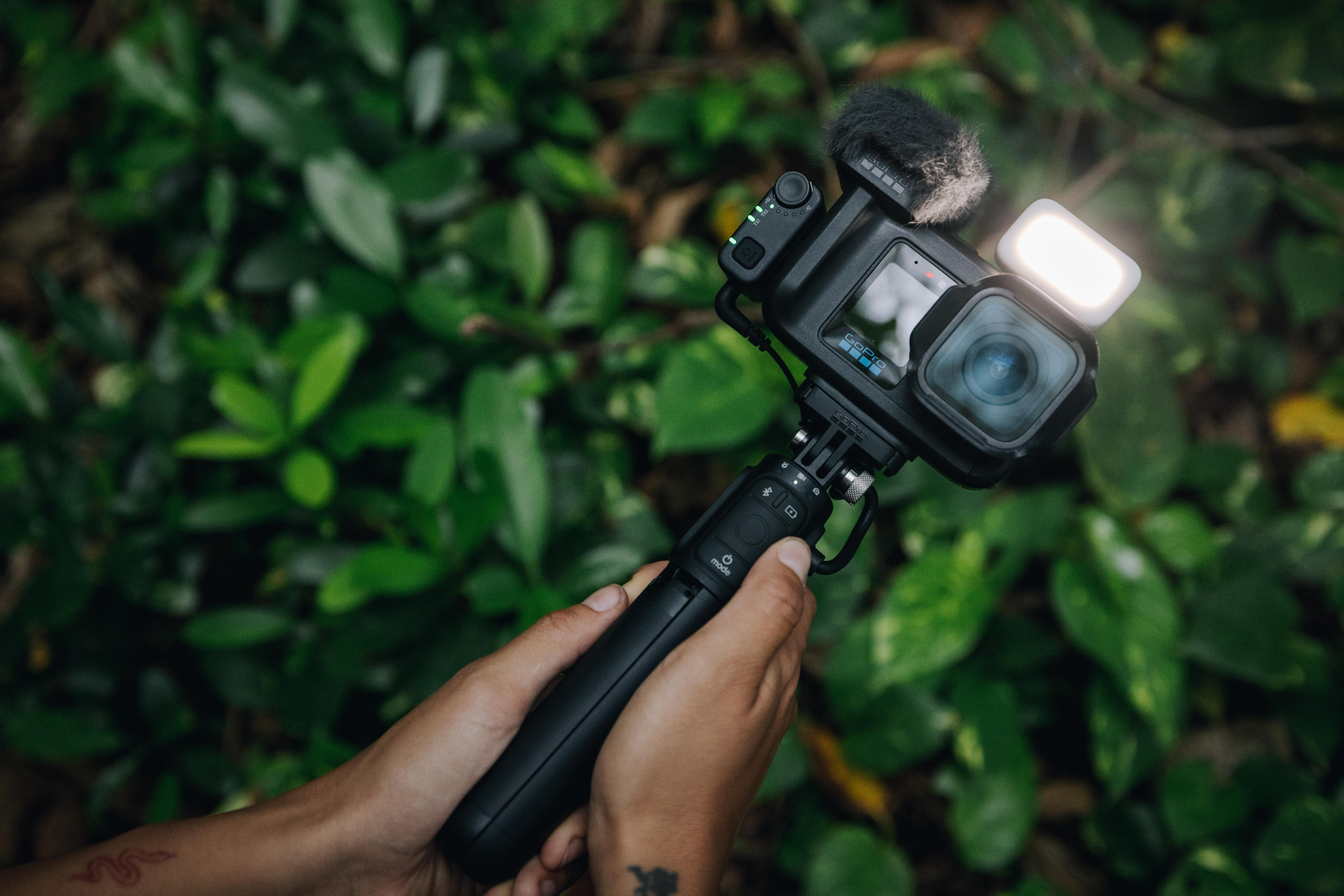 Eine Hand hält einen schwarzen Gimbal mit einer GoPro-Kamera und Mikrofon.