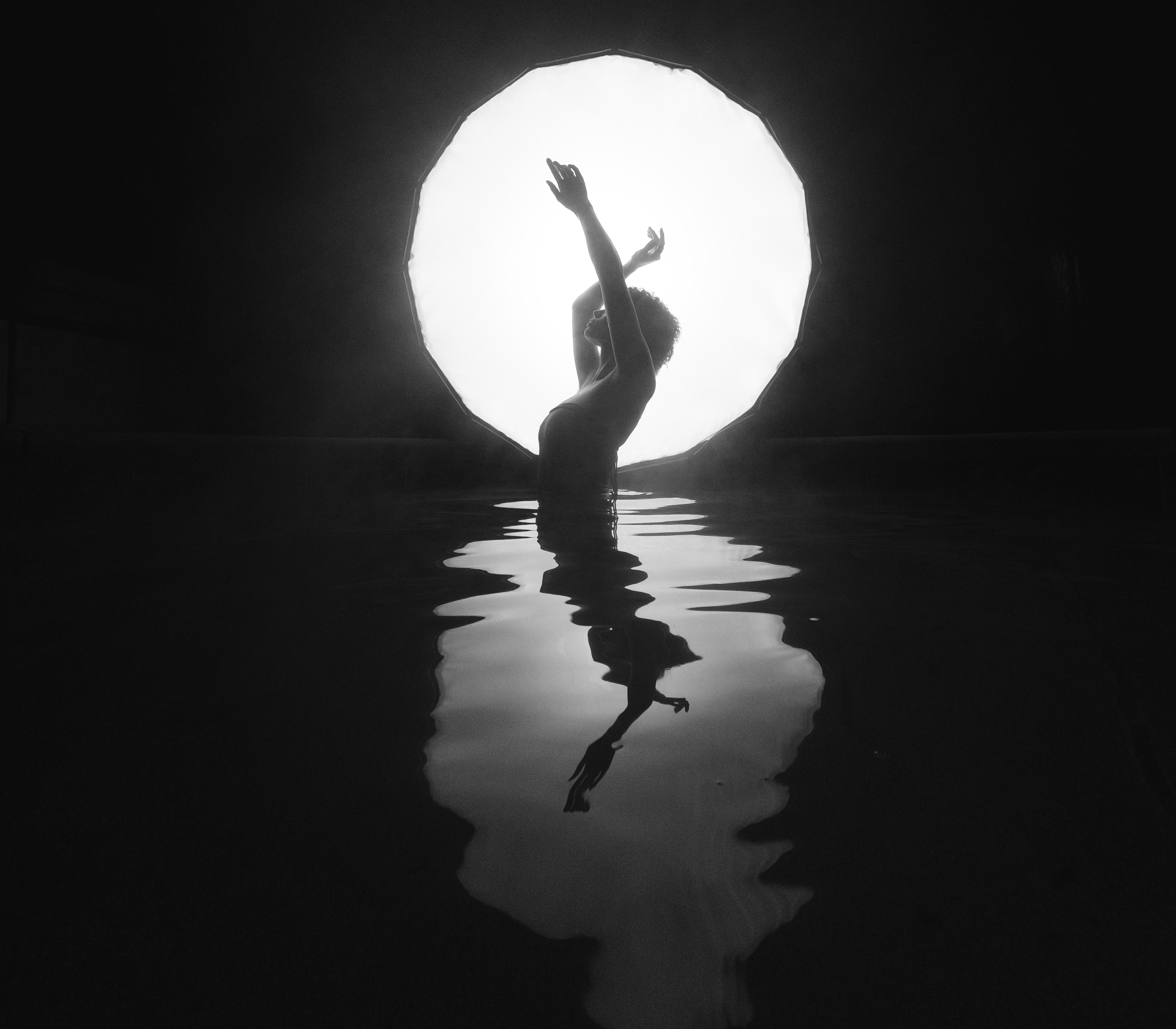 Eine Silhouette einer Person steht im Wasser vor einem hellen Kreis.