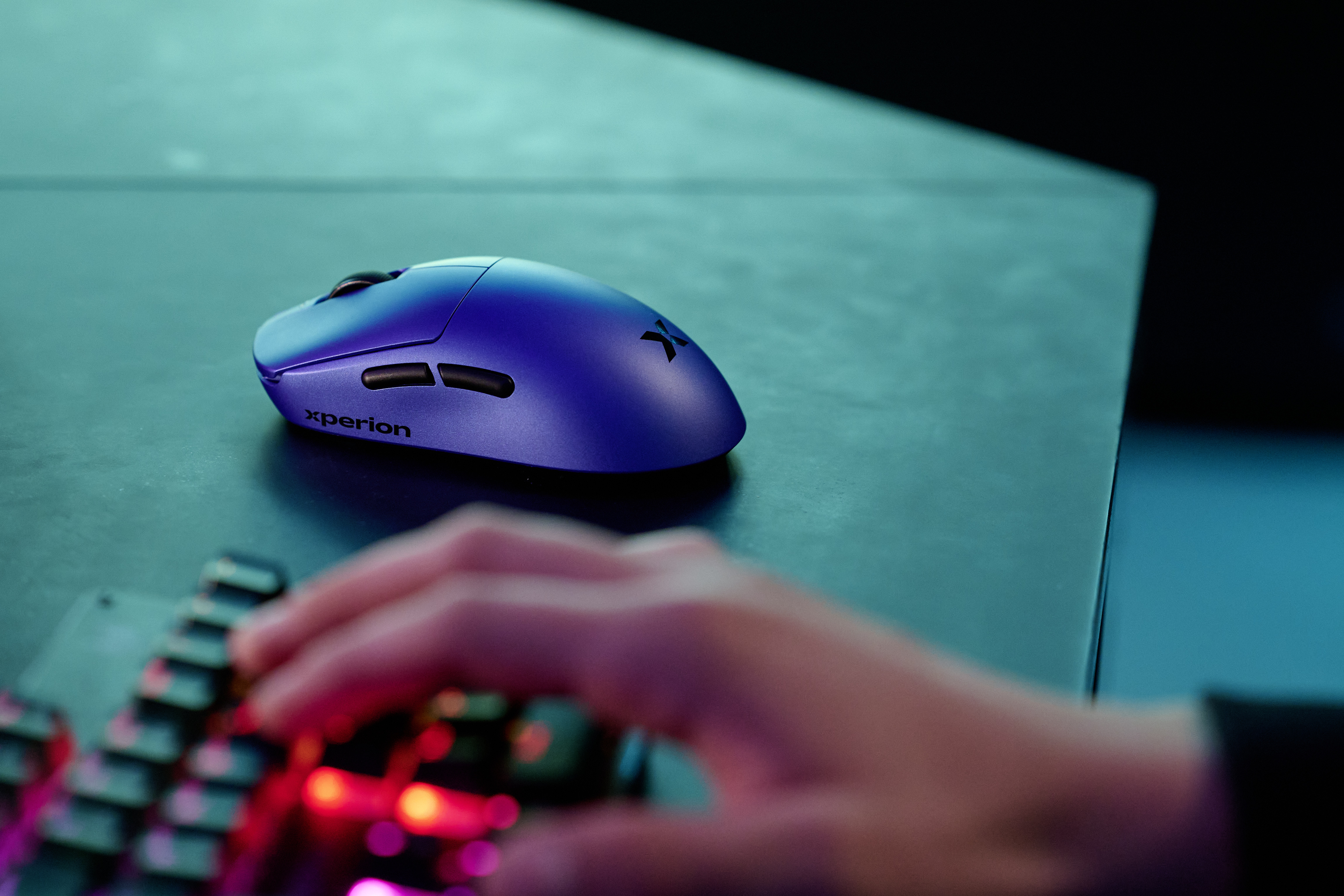 Eine blaue Gaming-Maus mit Xperion-Logo liegt auf einem dunklen Tisch.