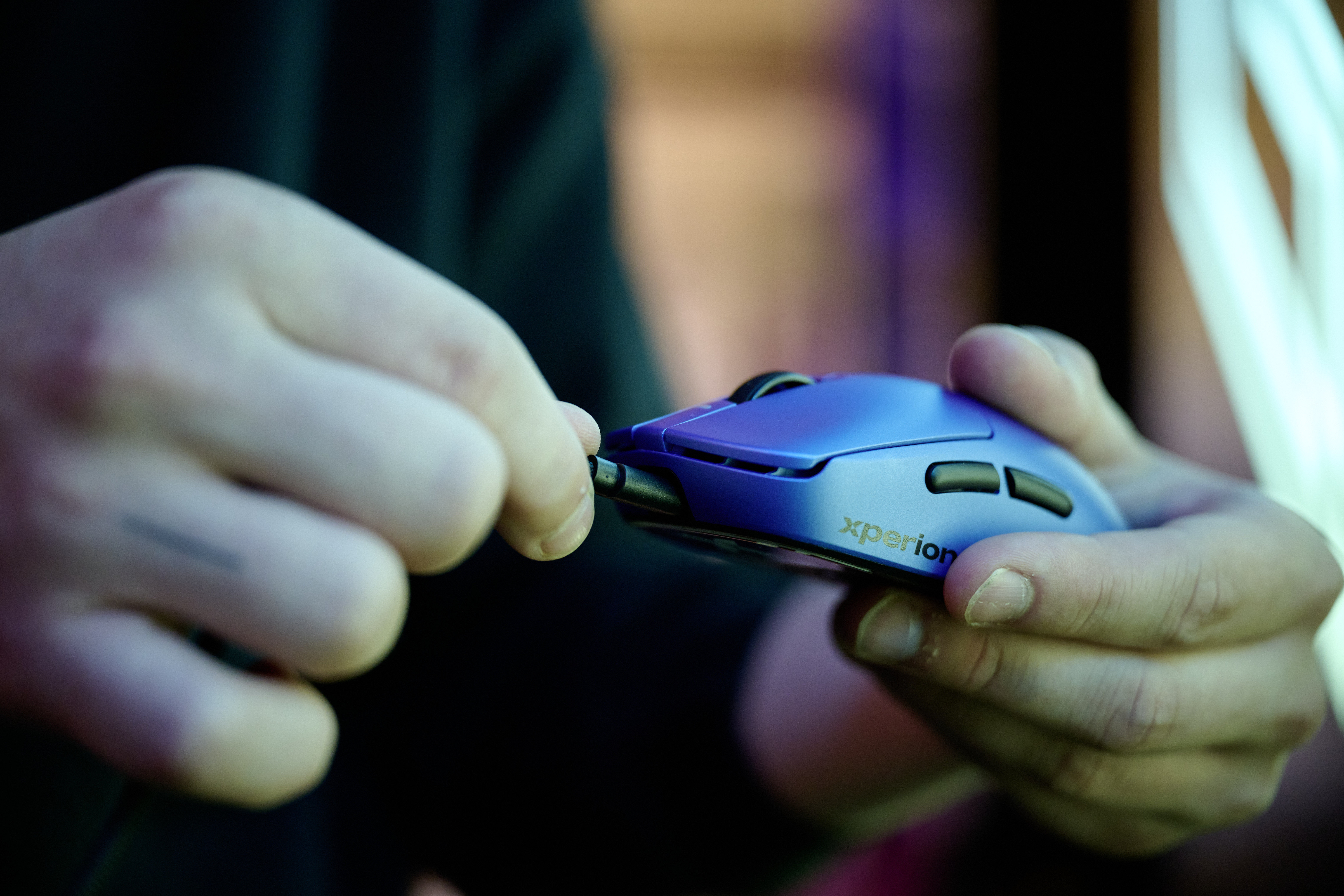 Eine Person hält eine blaue Computermaus mit einer Hand und steckt das Kabel mit der anderen ein.