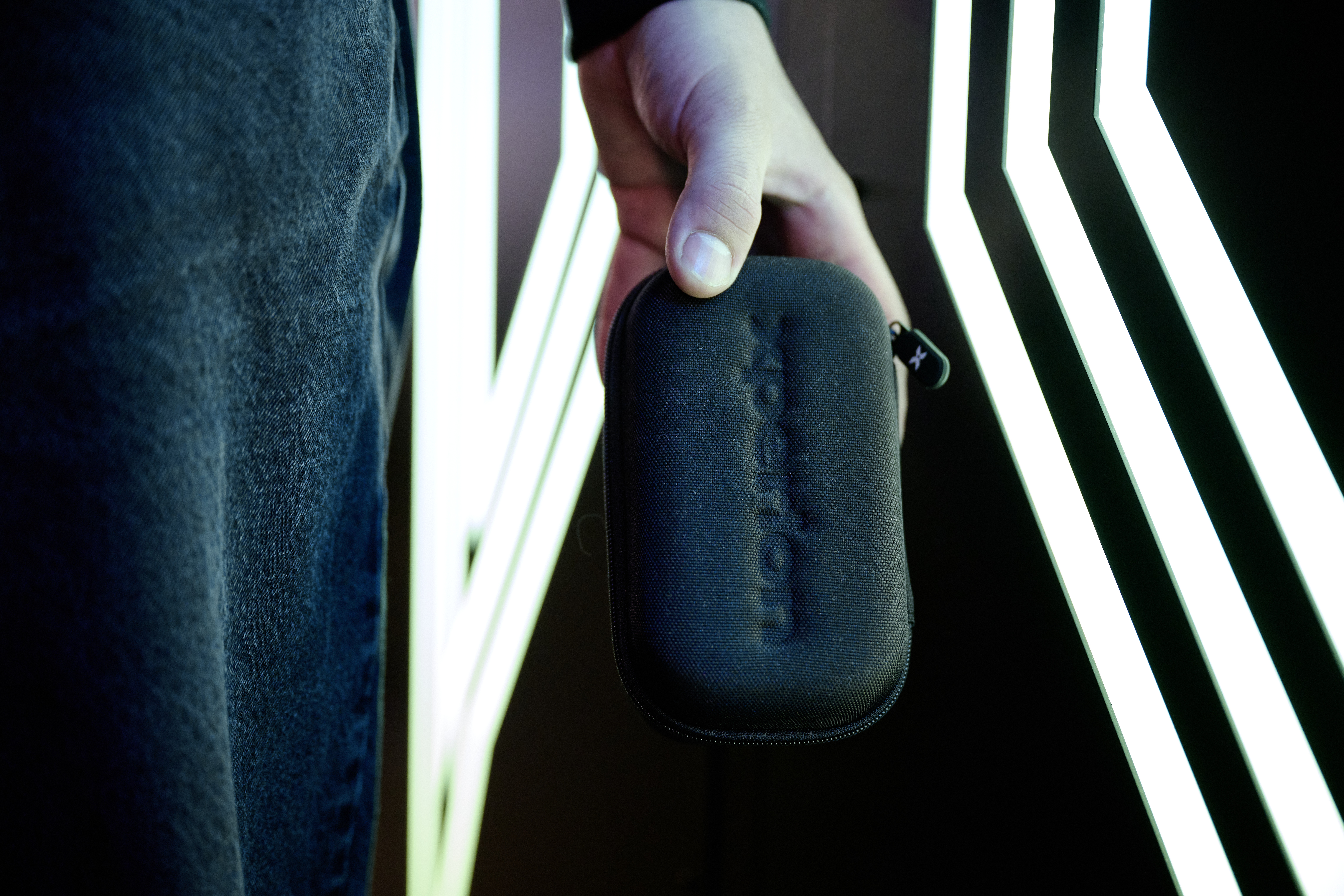 Eine Hand hält eine schwarze Tasche vor hellen Lichtern.