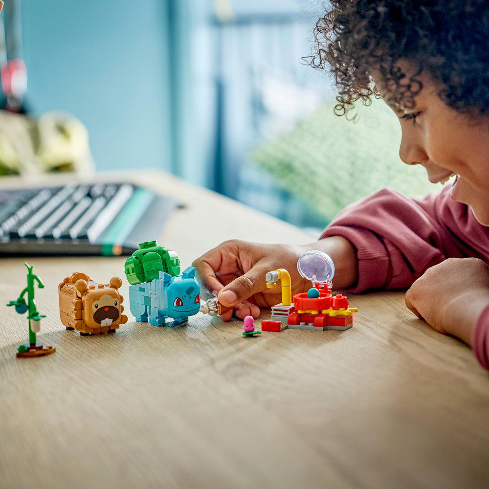 Kind spielt mit Lego-Pokémon: Braun, Grün und Blau auf einem Holztisch.