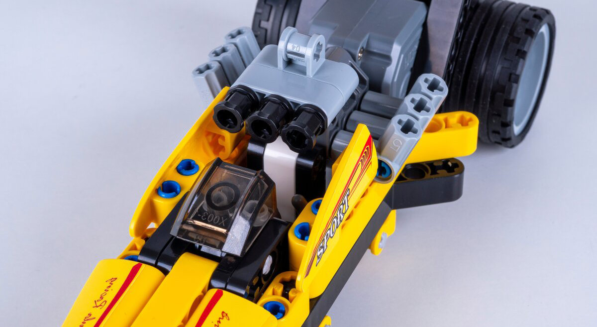 Egy sárga Lego versenyautó fekete és szürke alkatrészekkel, részletgazdag.