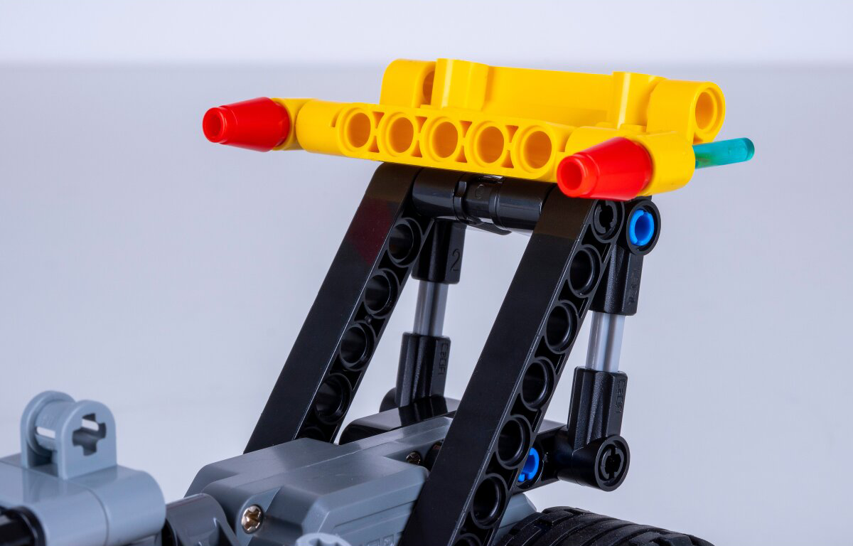 Egy sárga Lego gerenda piros végekkel fekkszik fekete támasztékokon.