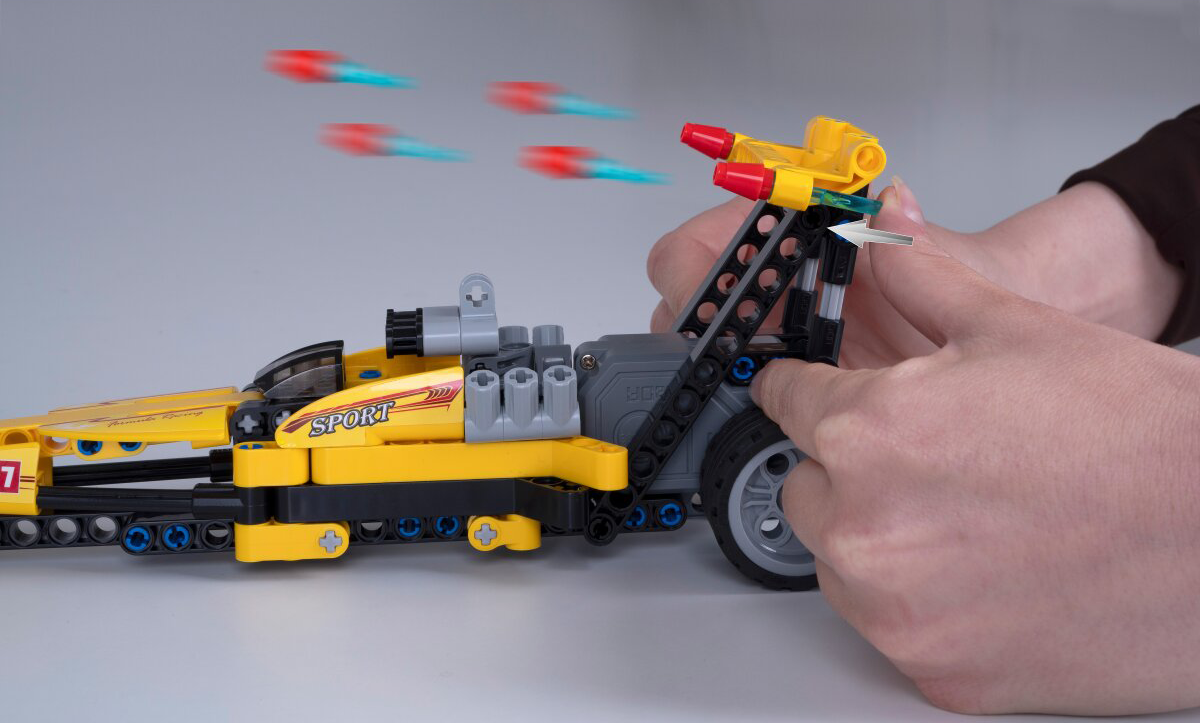 Kezek sárga Lego versenyautót szerelnek piros rakétákkal és kék csíkokkal.