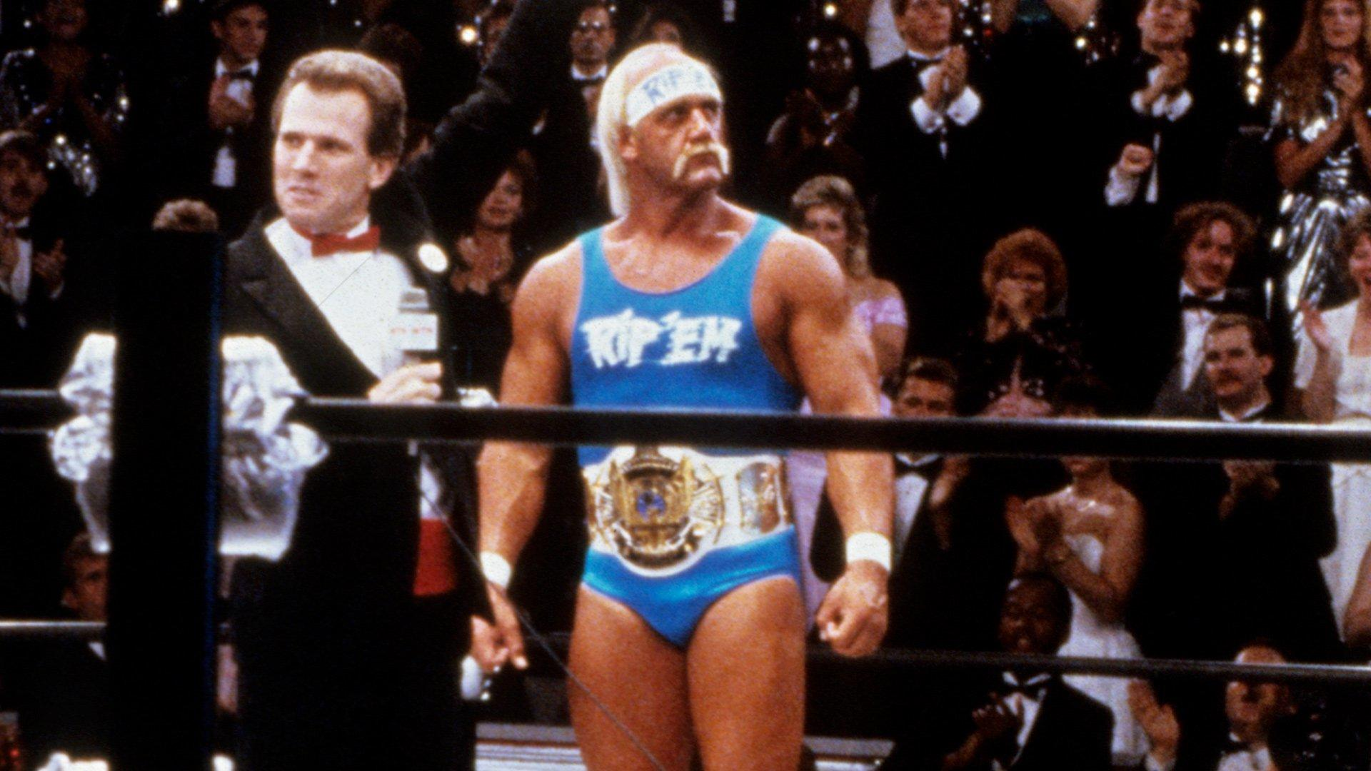 Ein Wrestler mit Bandana und blauem Tanktop steht im Ring vor einem Publikum.