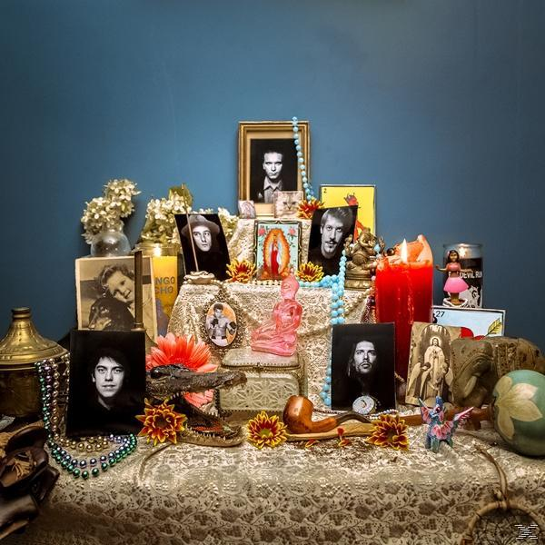 Ein Altar mit Fotos, Kerzen, Blumen und Schmuck auf einer Tischdecke.