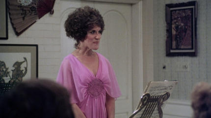 Frau in rosa Kleid mit kurzen Haaren steht vor einem Notenständer.