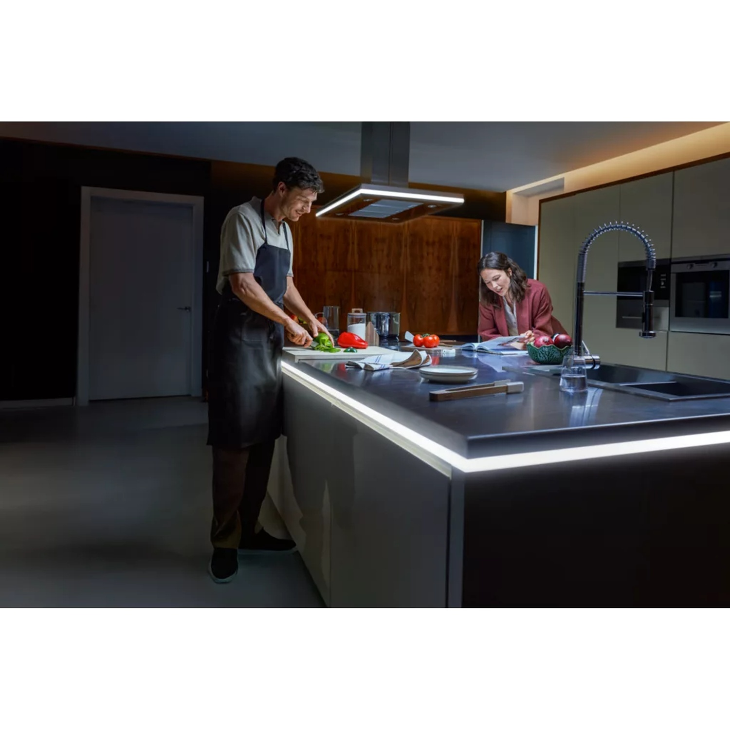 Homme cuisine, femme lit au comptoir de cuisine. Cuisine moderne.
