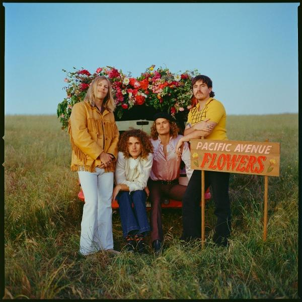 Vier Personen stehen vor einem Wagen voller Blumen. Ein Schild mit der Aufschrift "PACIFIC AVENUE FLOWERS" ist sichtbar.