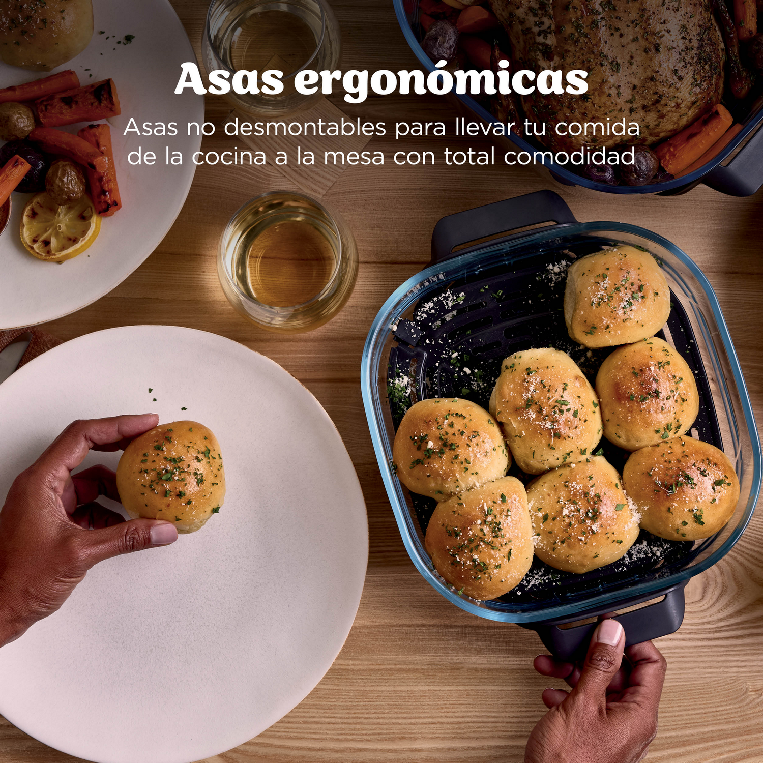 Una mano coloca un panecillo dorado en un plato blanco. En un recipiente de vidrio, más panecillos espolvoreados con hierbas.