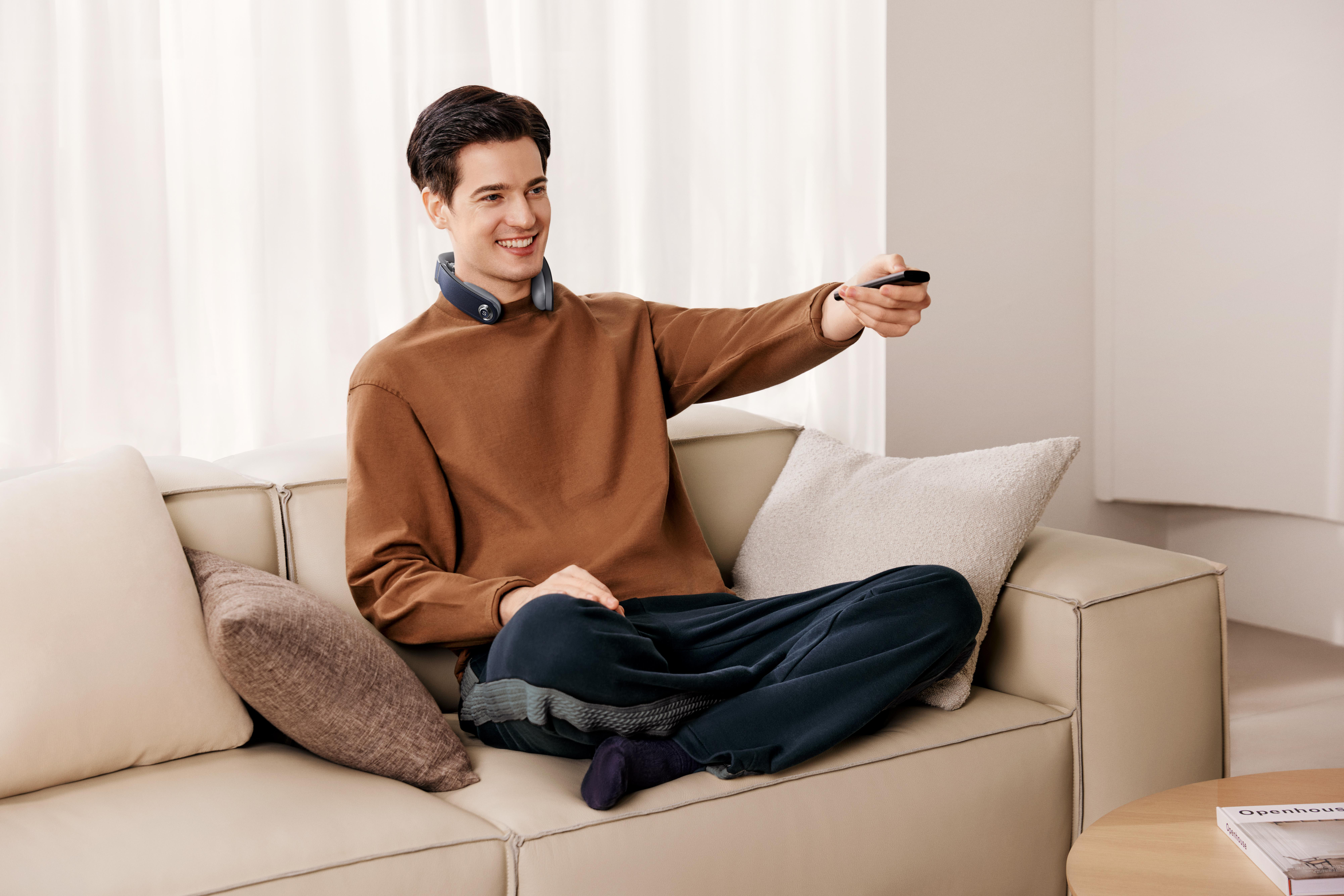 Ein Mann sitzt auf einem Sofa und hält eine Fernbedienung.