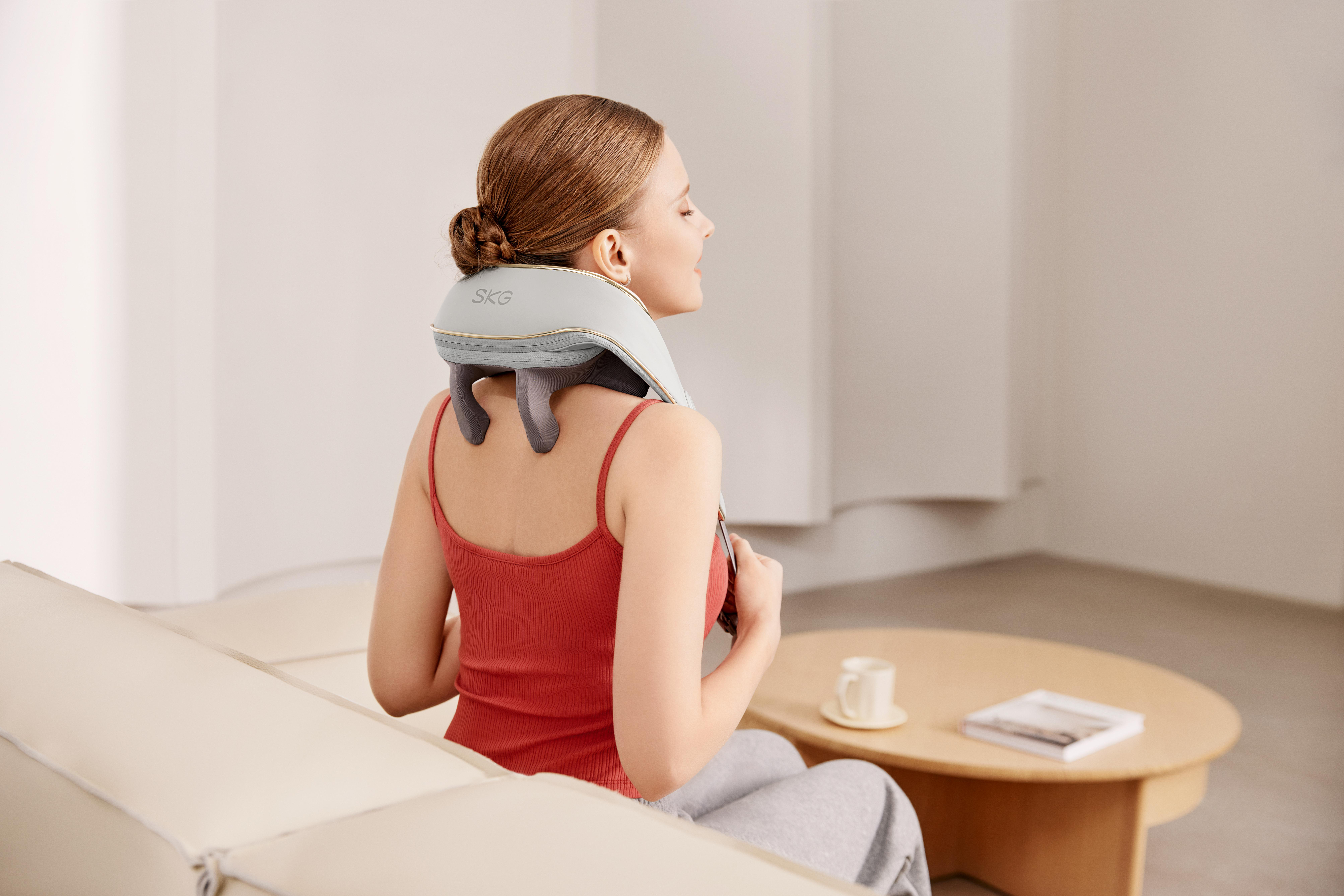 Eine Frau sitzt auf einem Sofa und benutzt ein Nackenmassagegerät.