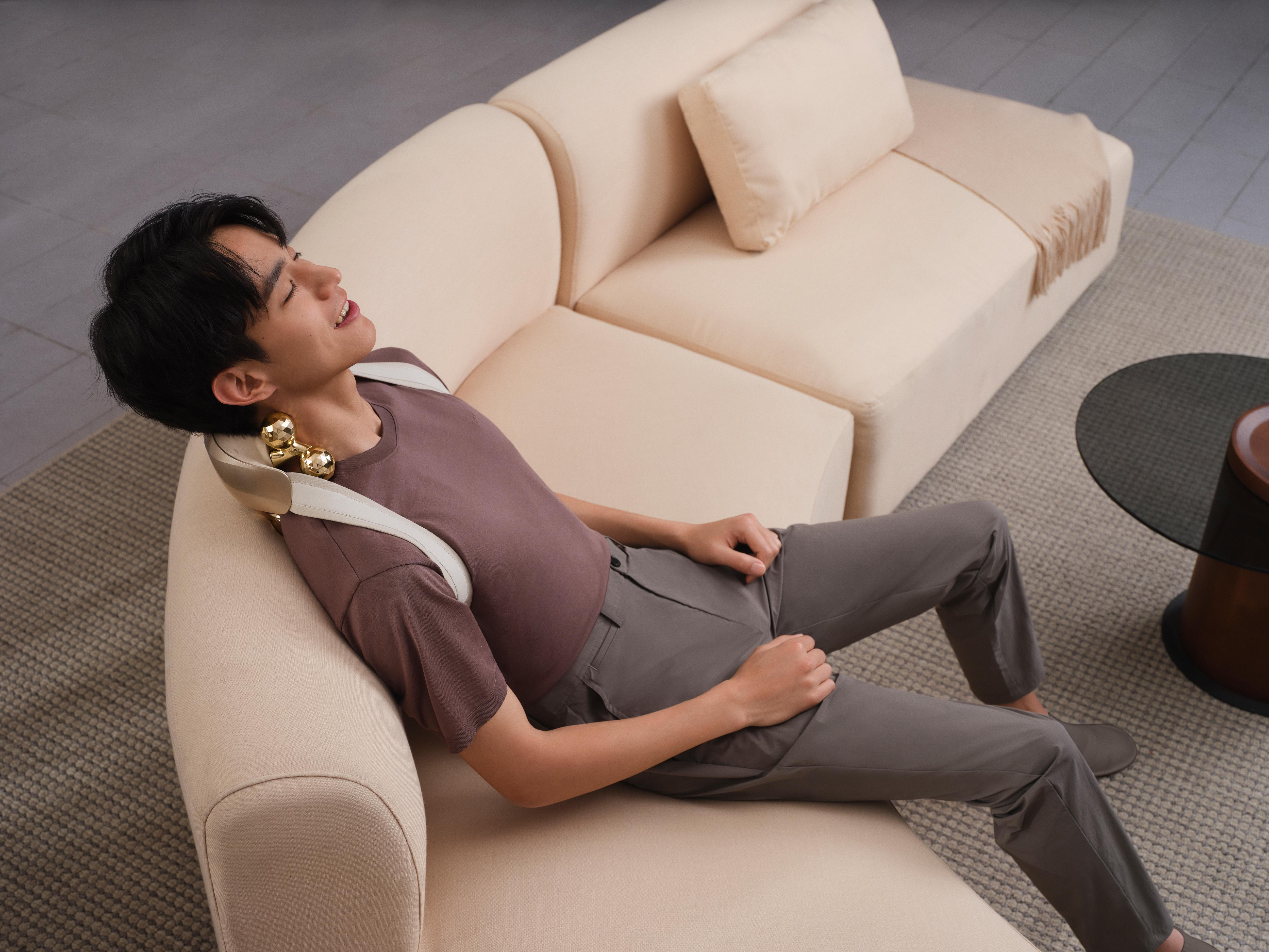 Mann entspannt auf einem Sofa mit Nackenmassagegerät.