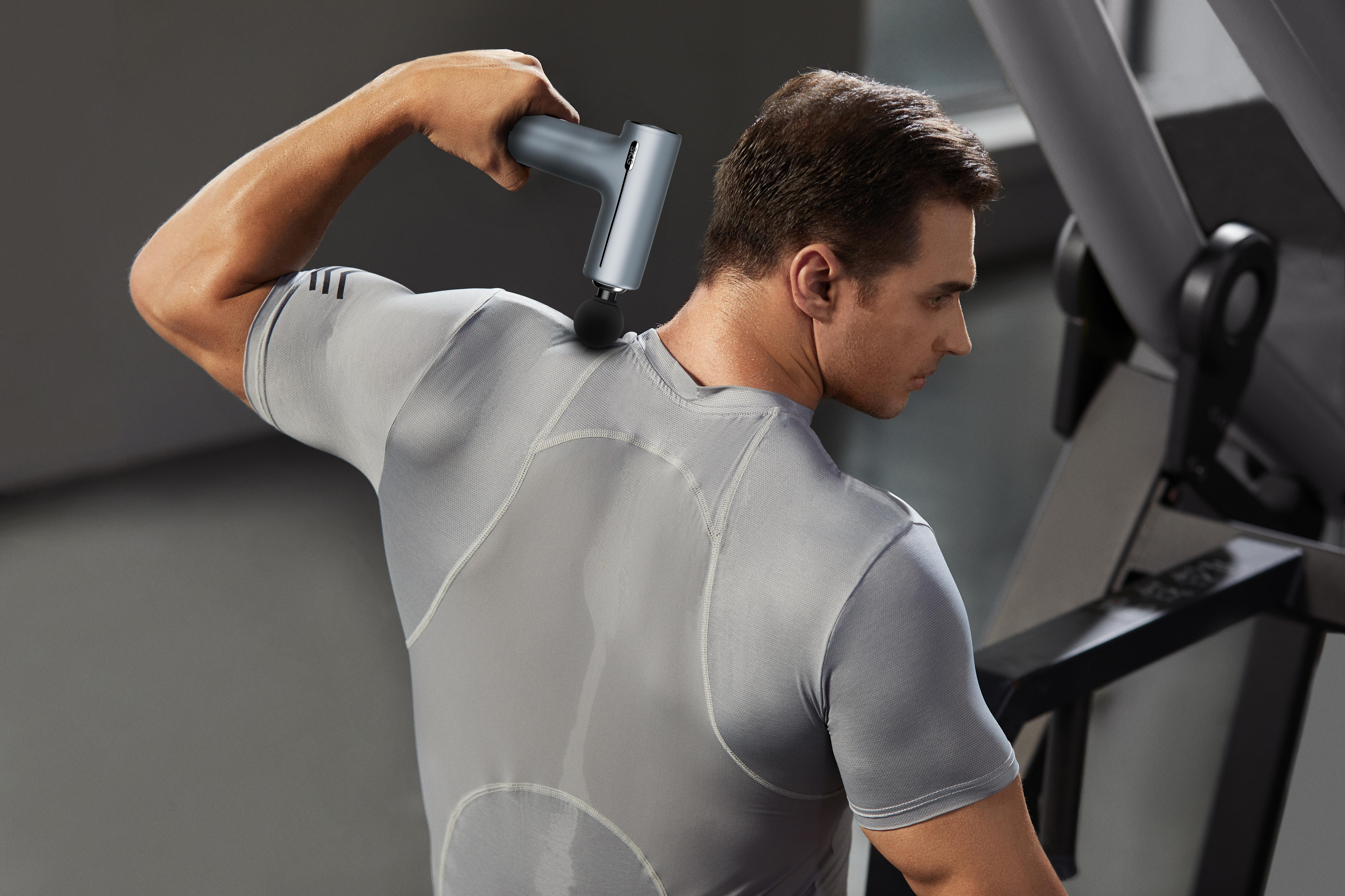 Mann massiert seinen Nacken mit einem Massagegerät im Fitnessstudio.
