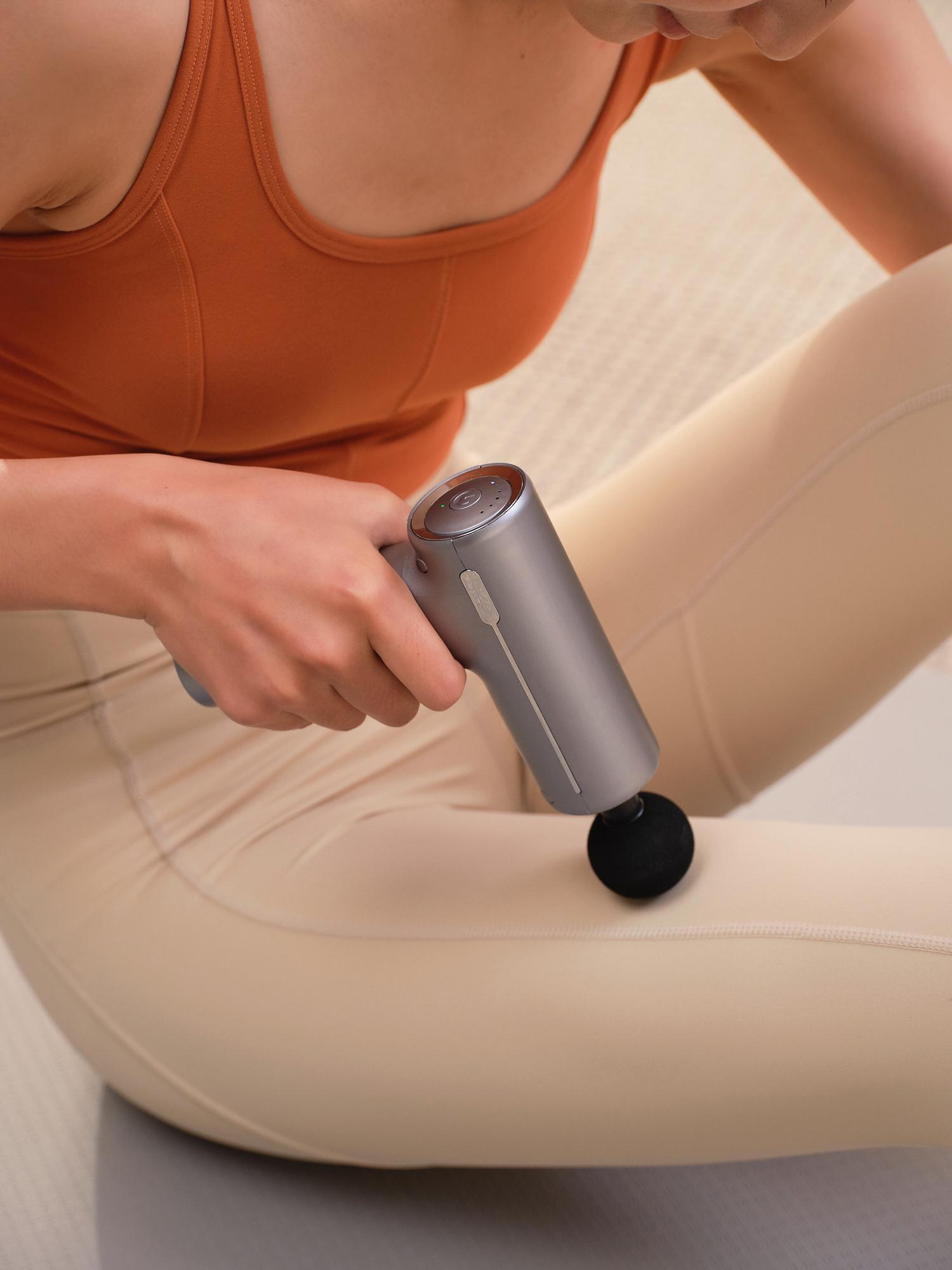 Eine Person in Sportkleidung benutzt eine Massagepistole am Bein.