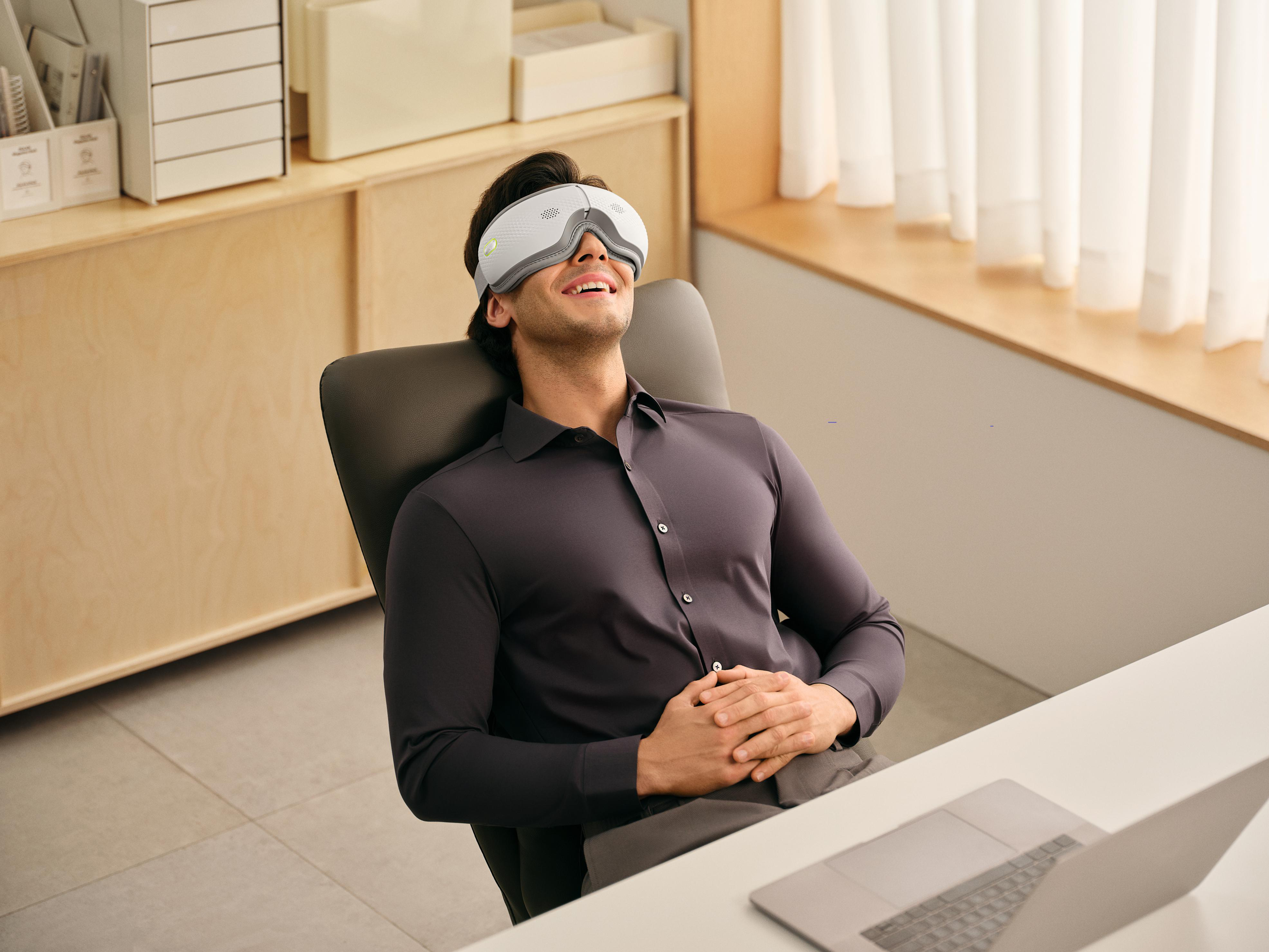 Mann mit Massagebrille sitzt am Schreibtisch und entspannt sich.