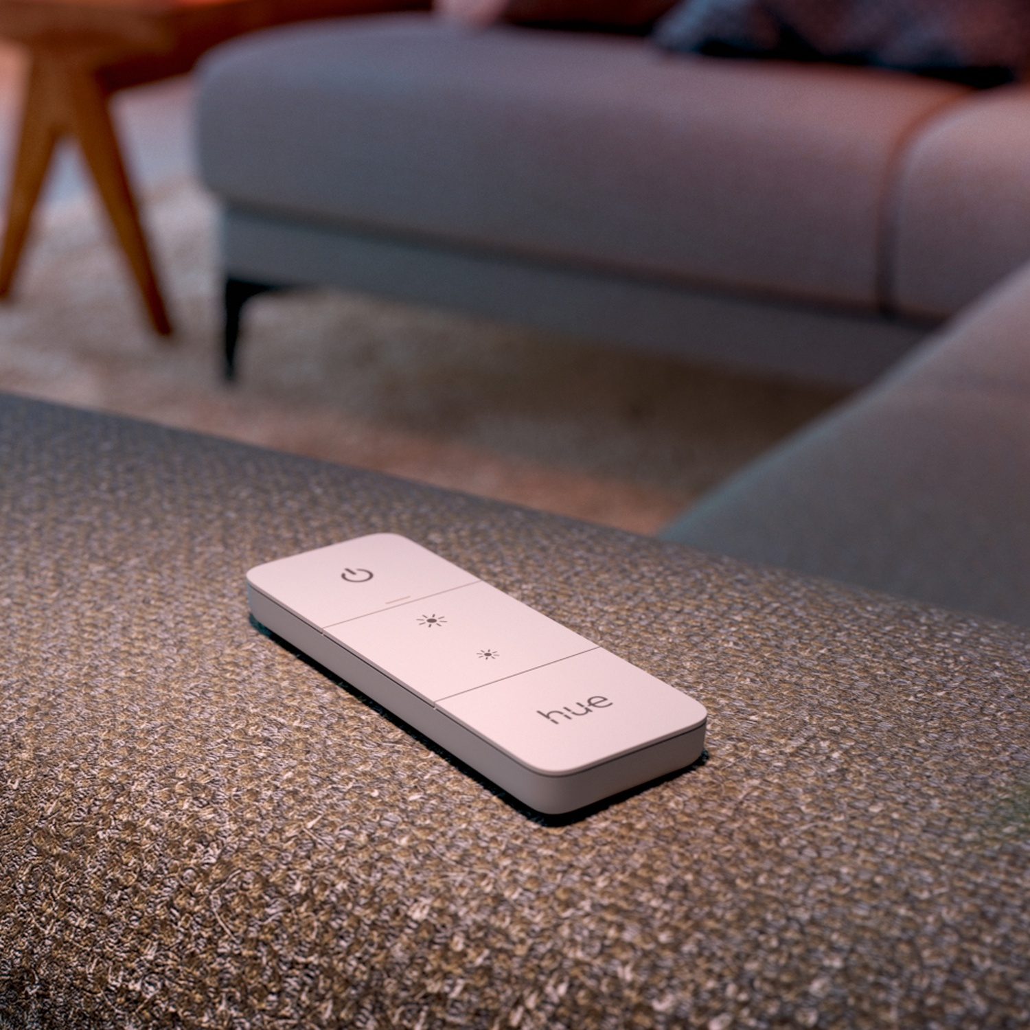 Une télécommande HUE blanche est posée sur un canapé en tissu gris-brun.