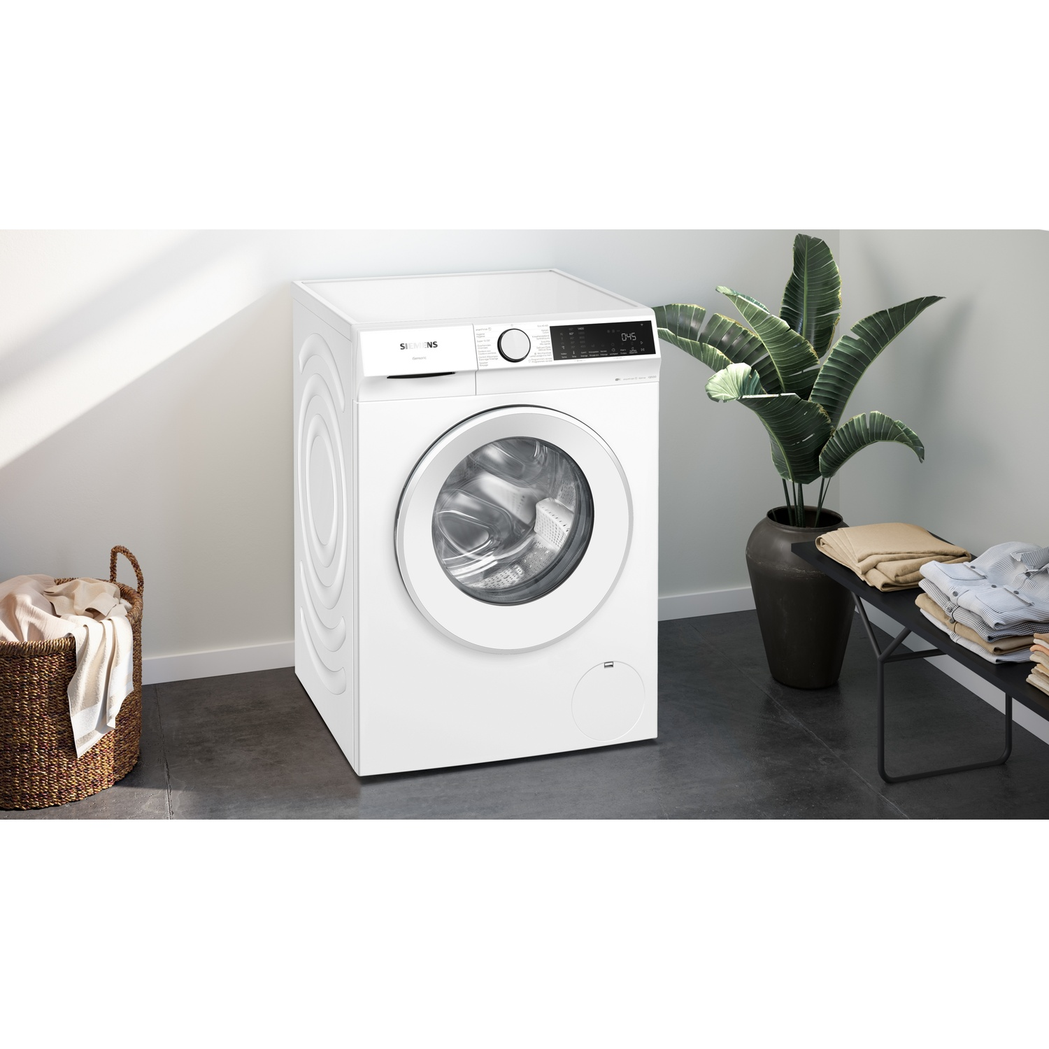 Machine à laver blanche avec panier à linge et plante.