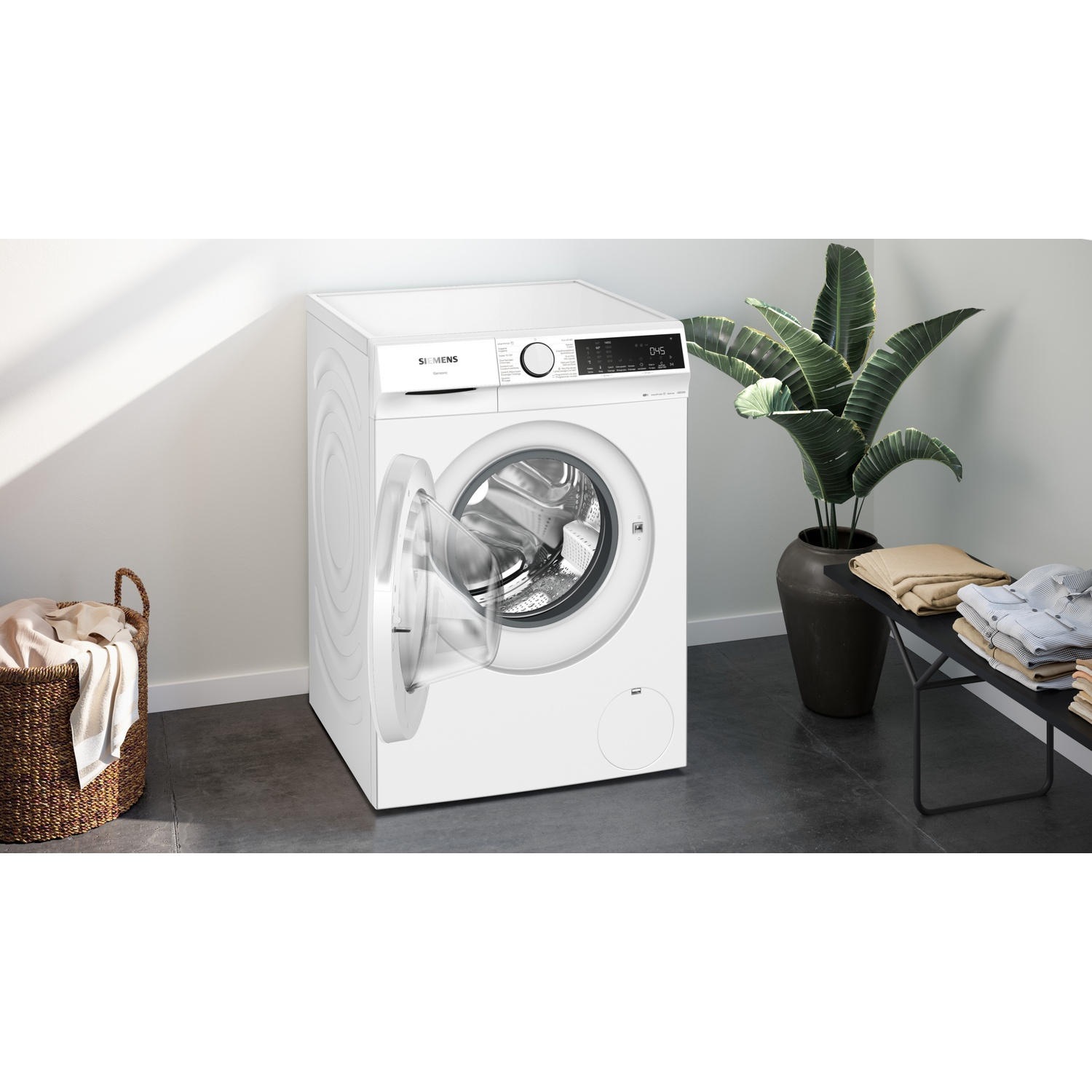 Une machine à laver Siemens blanche, porte ouverte, se trouve à côté d'un panier à linge.