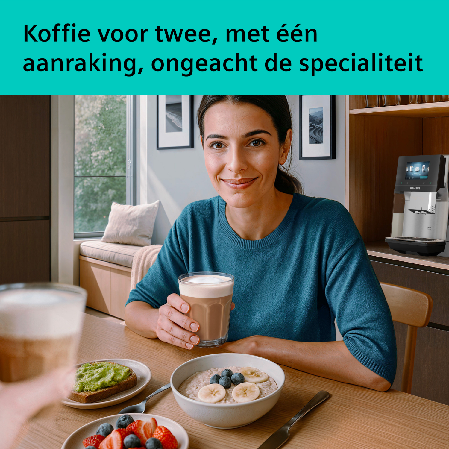 A woman sits at a table holding a drink. Coffee and breakfast are on the table.