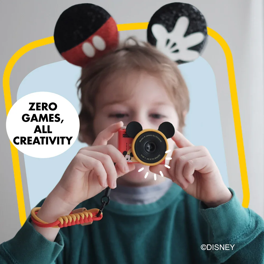 Egy gyerek Mickey-fülekkel Mickey-témájú kamerát tart. Szöveg: Zero Games, All Creativity.