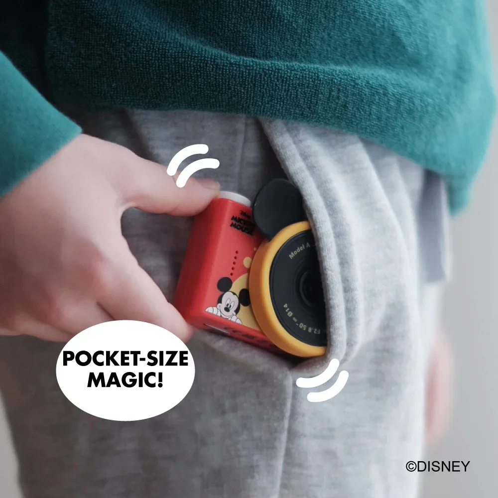 Egy kéz egy piros Mickey egeres kamerát dug egy szürke zsebbe.