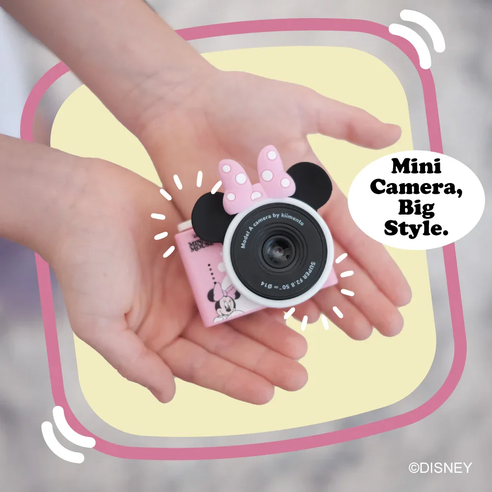 Kezek egy rózsaszín Minnie Mouse mini fényképezőgépet tartanak fülekkel és masnival.