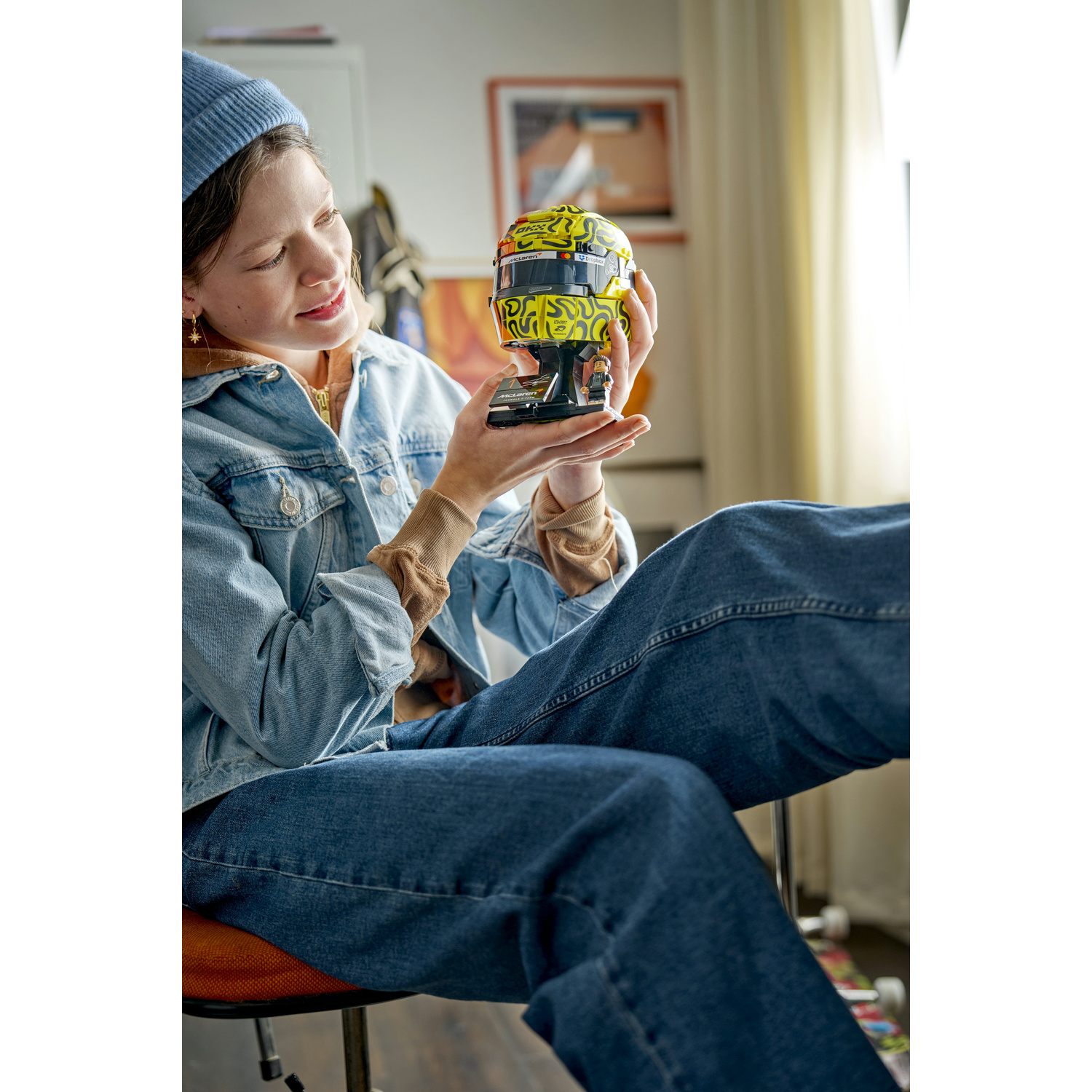 Una donna con cappello blu e giacca di jeans tiene un casco giallo.