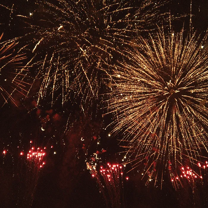 Arany és piros tűzijáték robban az éjszakai égbolton.