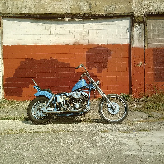 Egy kék chopper motor áll egy piros és fehér téglafal előtt.