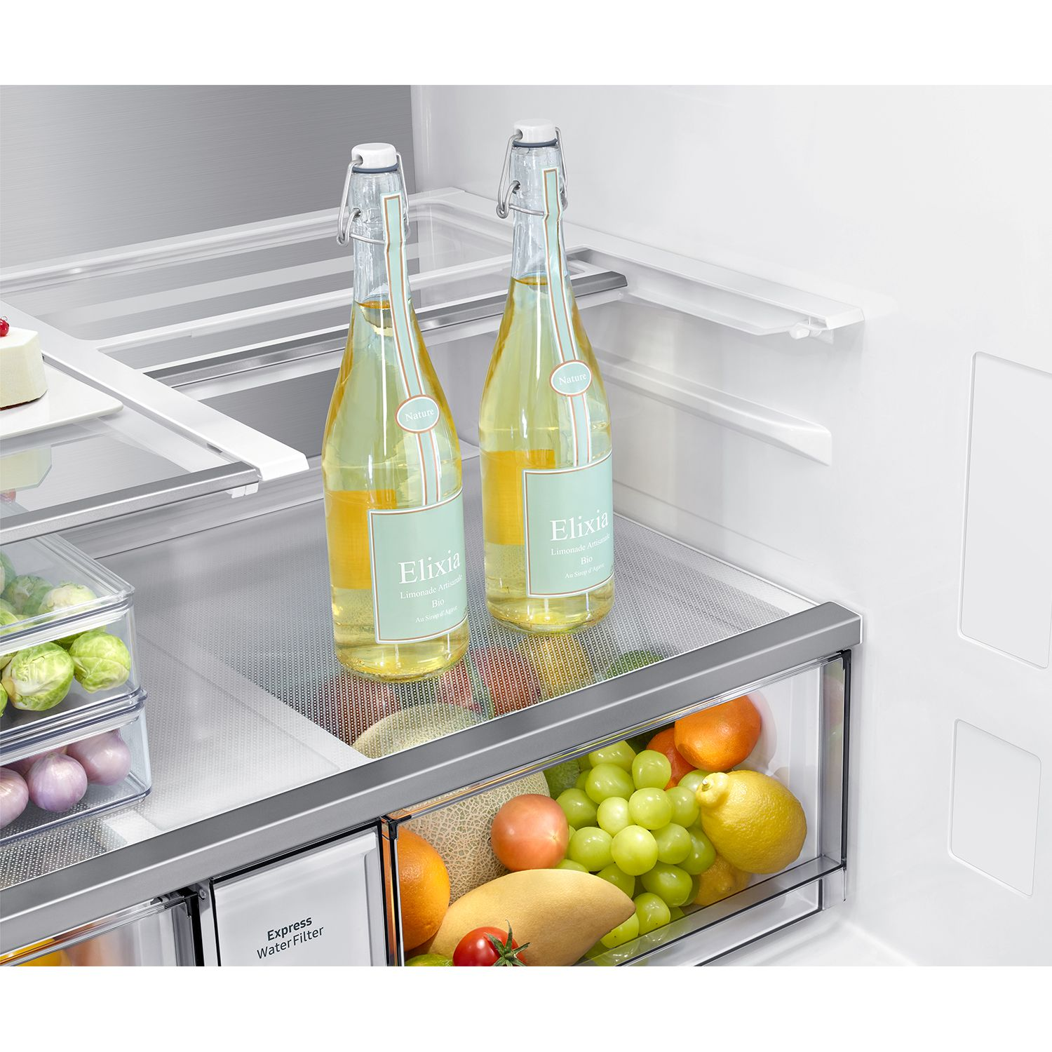 Dentro de un refrigerador, dos botellas de limonada Elixia están en un estante sobre un cajón de frutas.