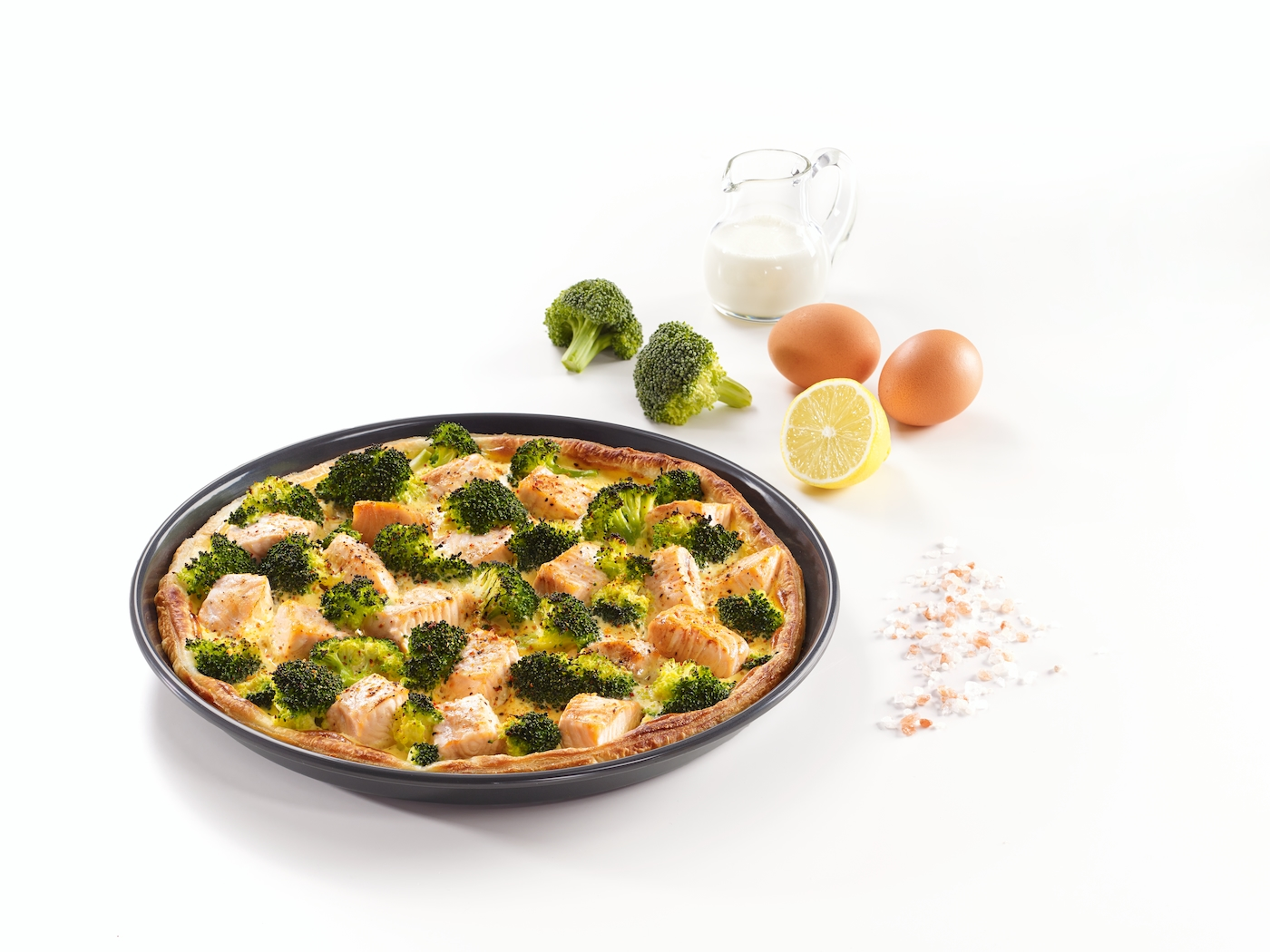 Lachs-Brokkoli-Quiche in dunkler Pfanne mit Zitrone, Eiern, Milch und Salz.