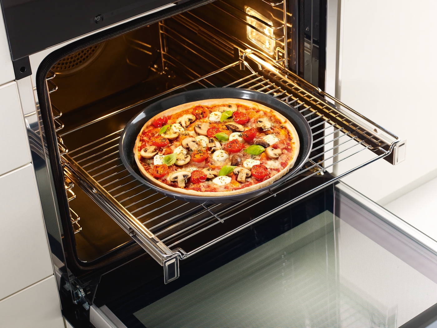 Eine Pizza mit Pilzen, Tomaten und Mozzarella wird im Ofen gebacken.