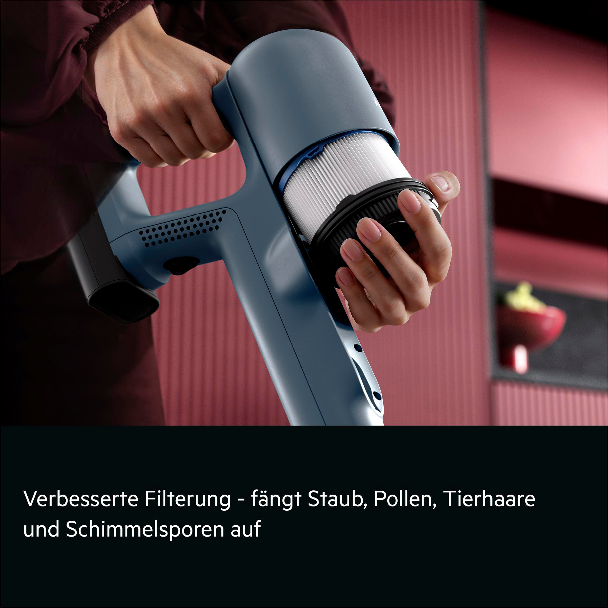 Eine Person tauscht einen blauen Staubsaugerfilter aus. Der Hintergrund ist rot.