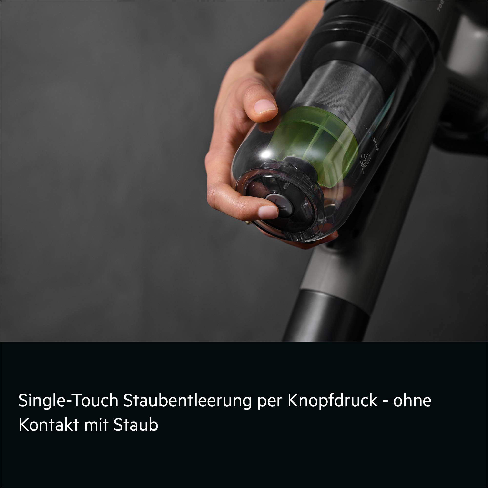 Eine Hand drückt einen Knopf an einem transparenten Staubbehälter mit grünem Inhalt.